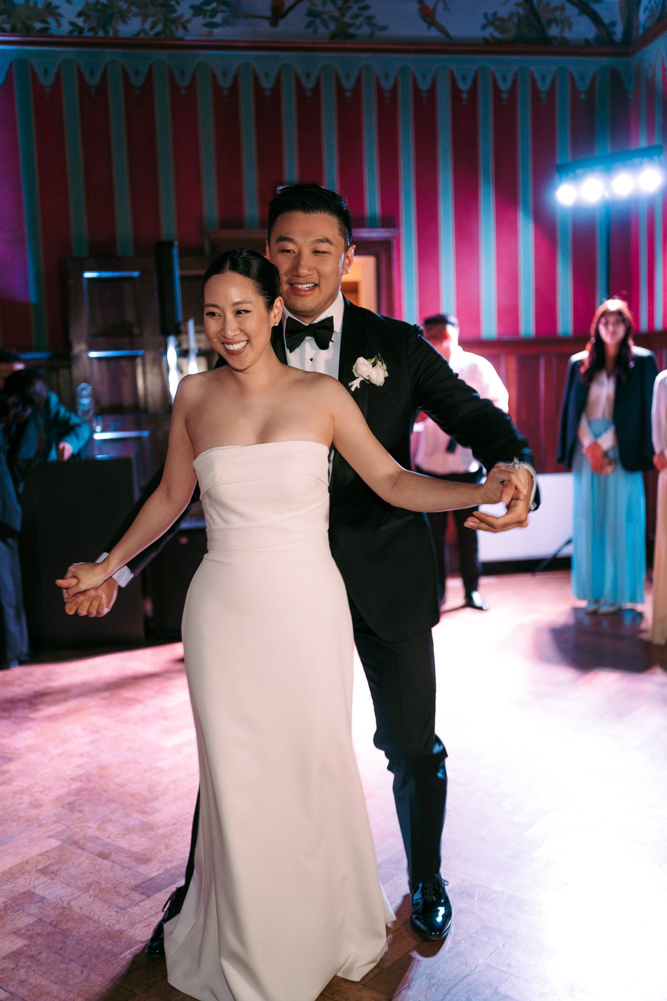 A couple performs their first dance at a wedding reception with pink and blue lighting on the dance floor.