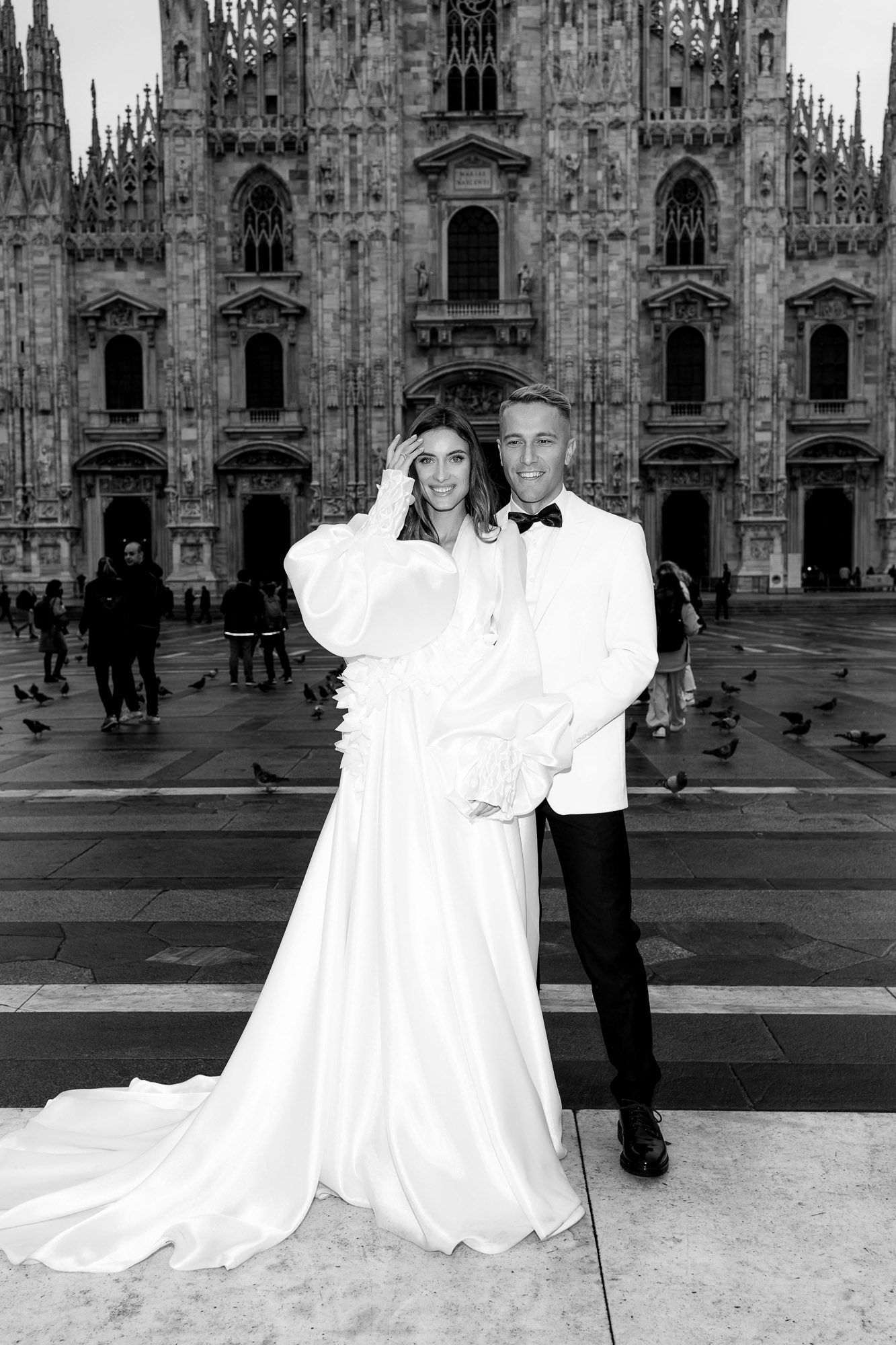 A black and white photo series showing figures in white dresses posing in front of Milan Cathedral in Italy.