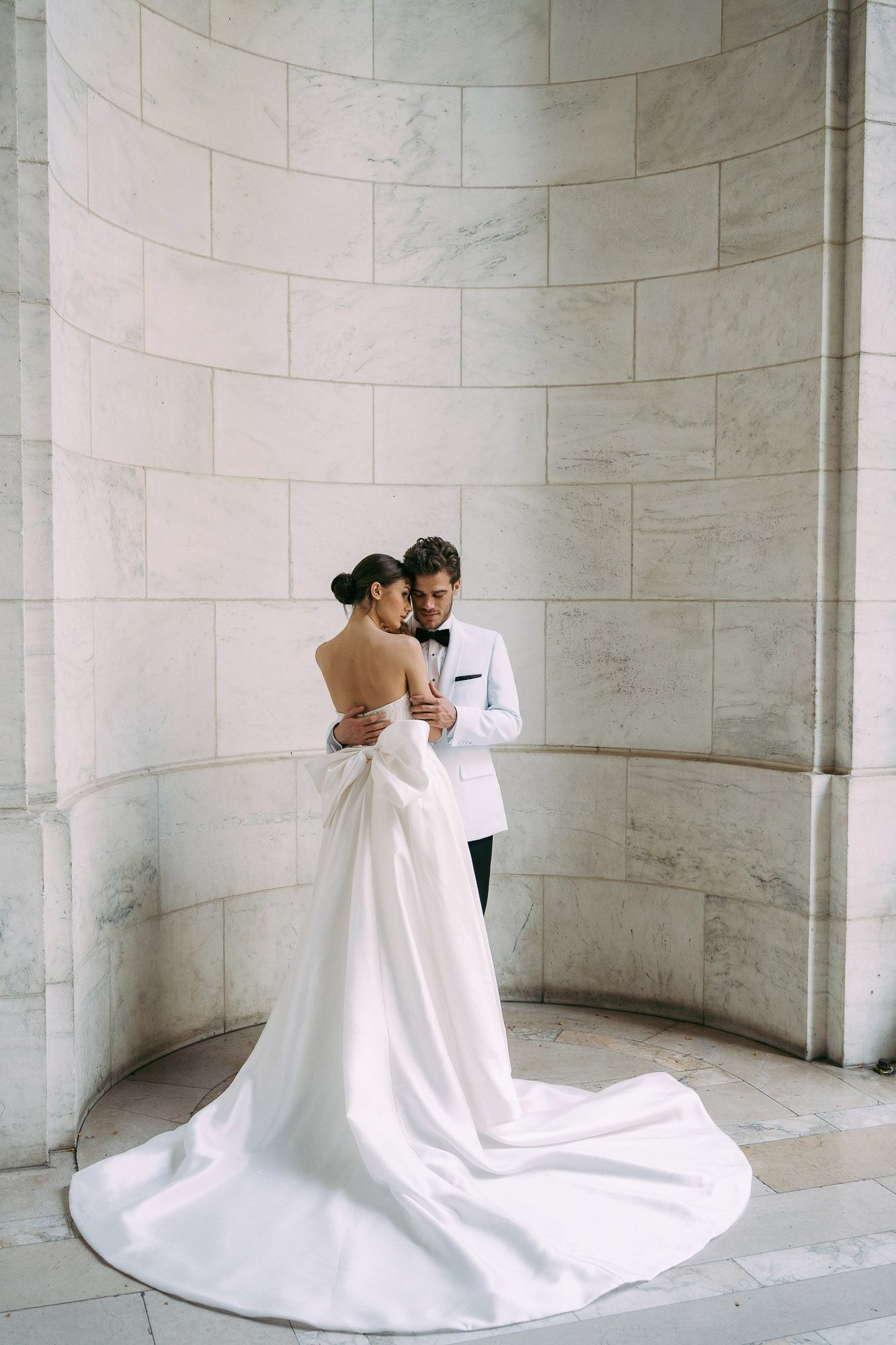A romantic wedding photo series showing a couple embracing in an elegant marble rotunda with flowing white dress details.
