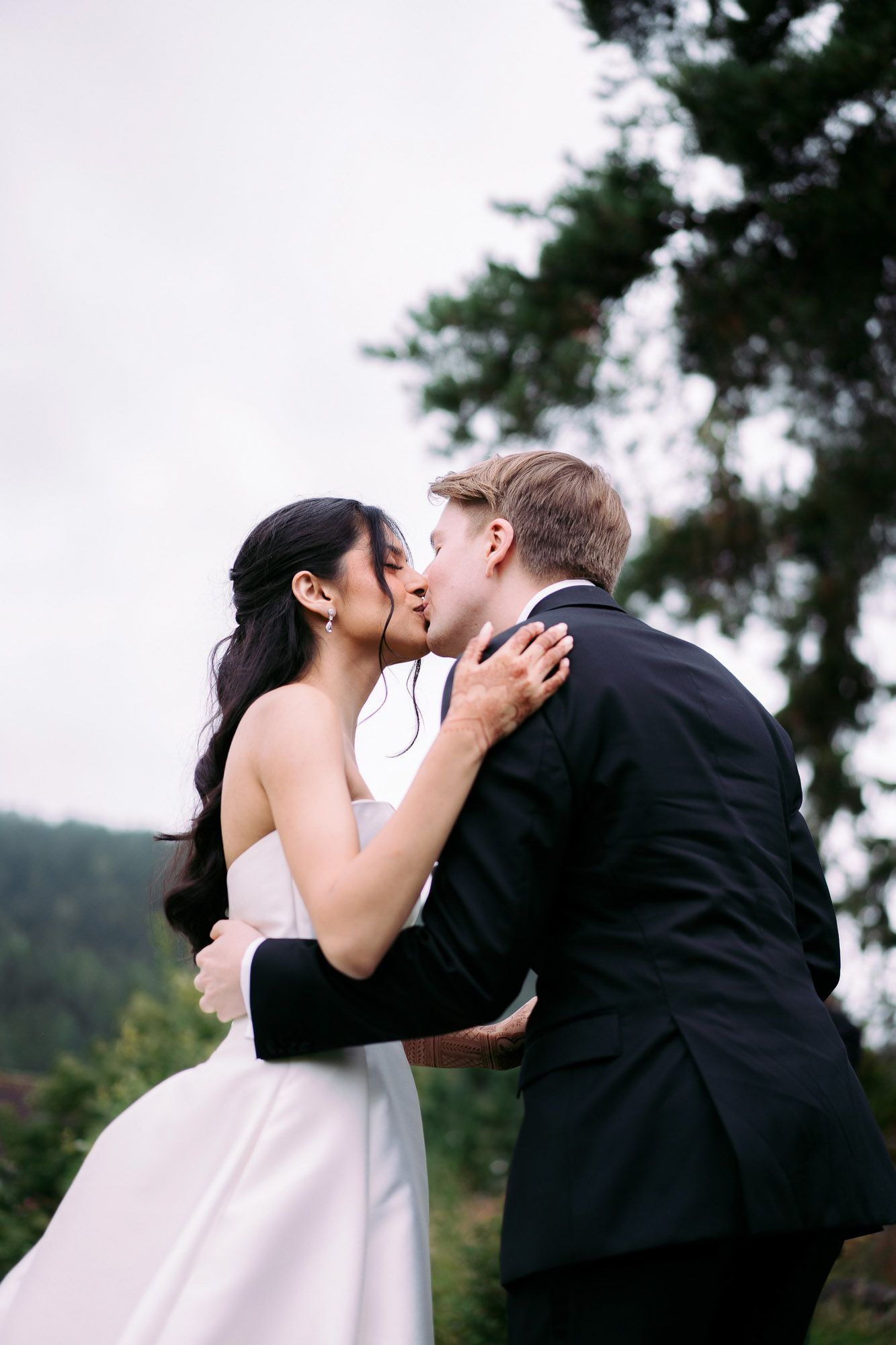 A romantic sequence of four wedding photos showing a couple sharing a tender kiss outdoors with trees in the background.