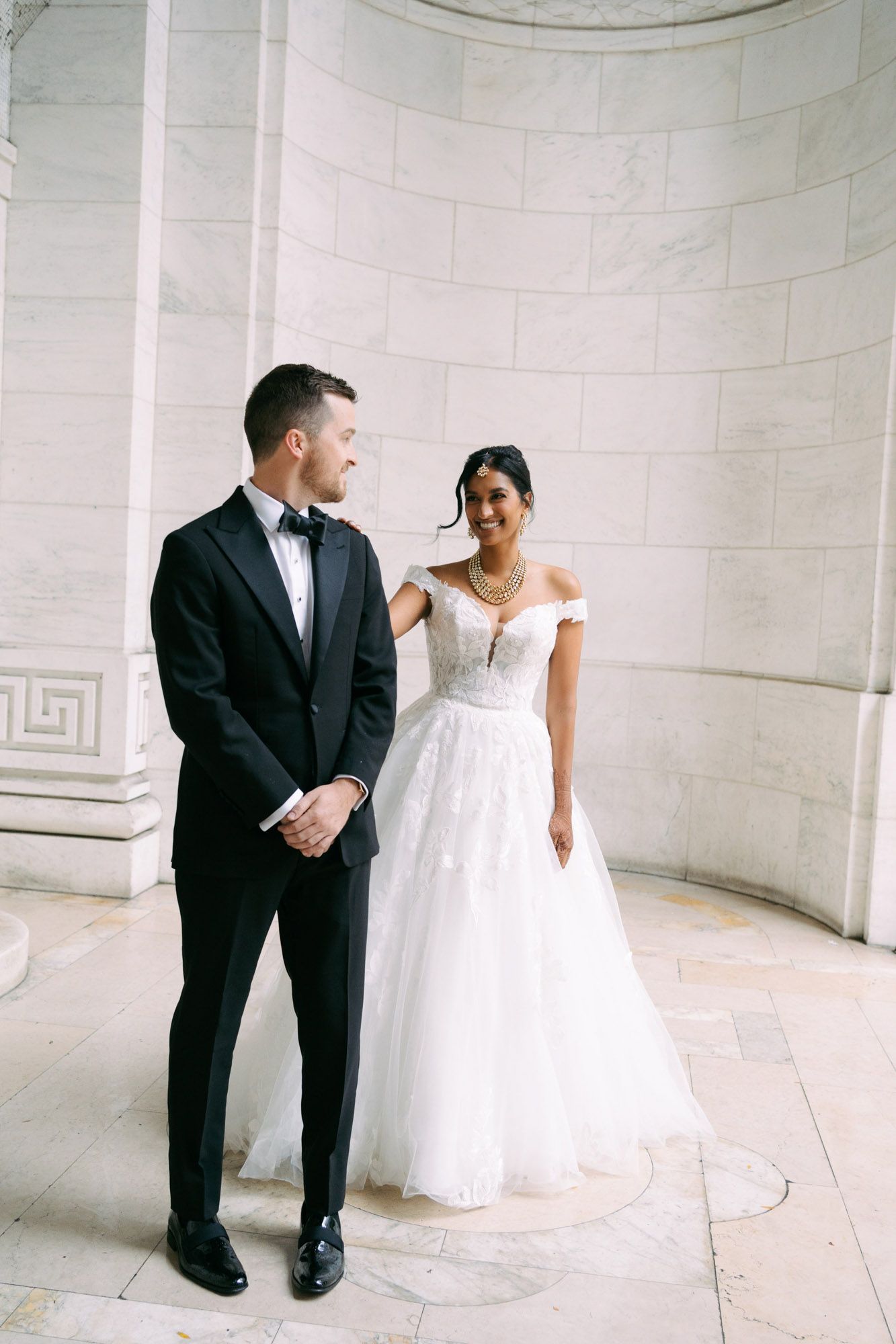 A romantic wedding photo series showing a couple in formal attire sharing tender moments in a bright marble corridor.