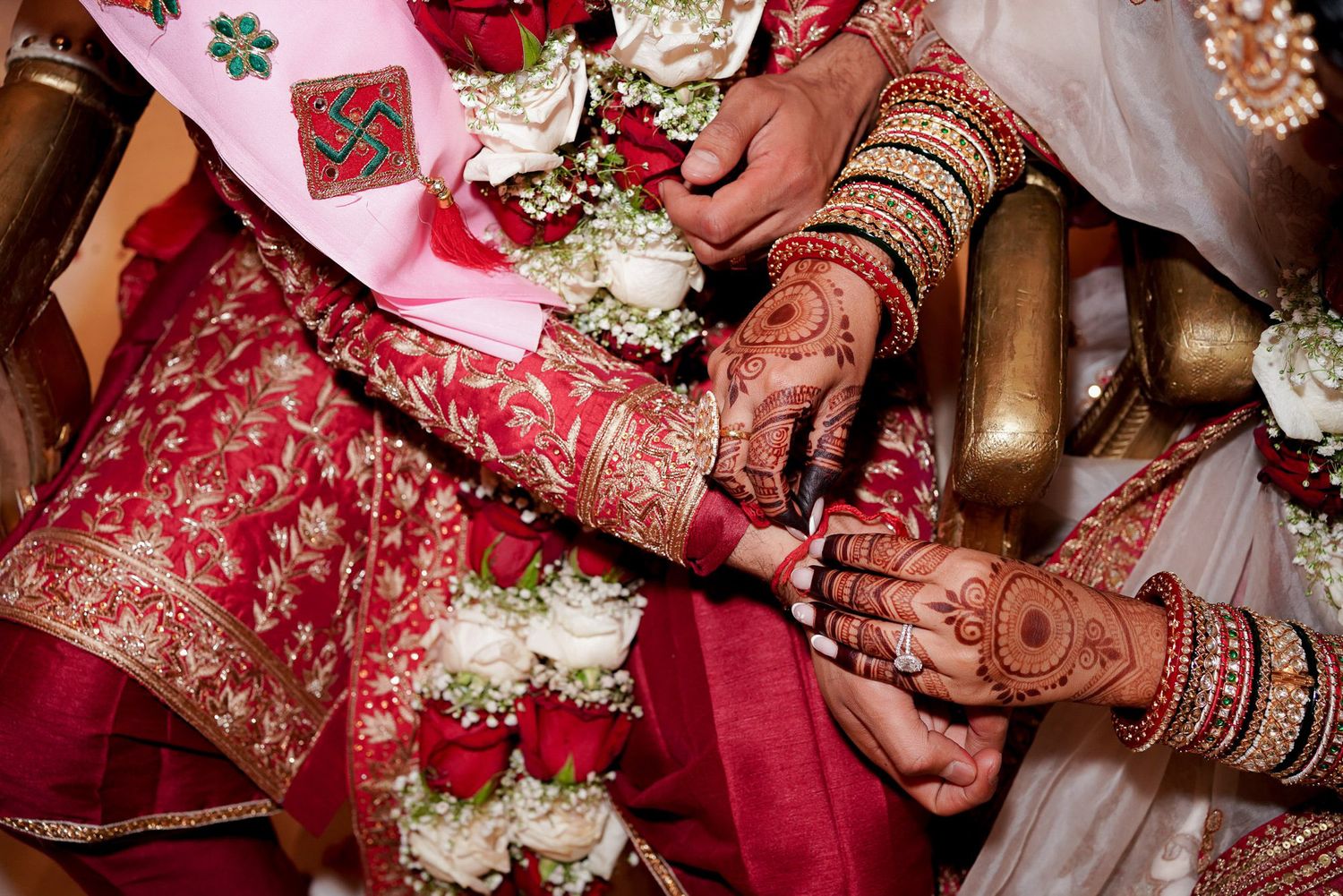 Hands adorned with intricate henna designs hold delicate flowers and jewelry during a traditional wedding ceremony.