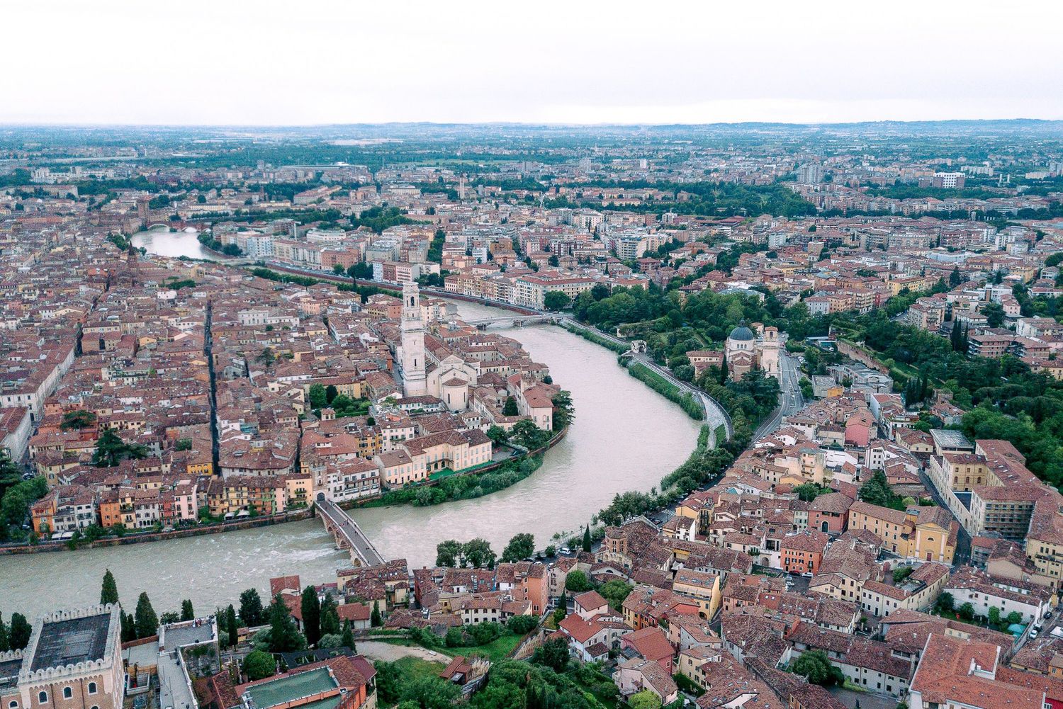 Aerial panoramic view of the historic city of Verona with its winding river, red rooftops, and ancient architecture.