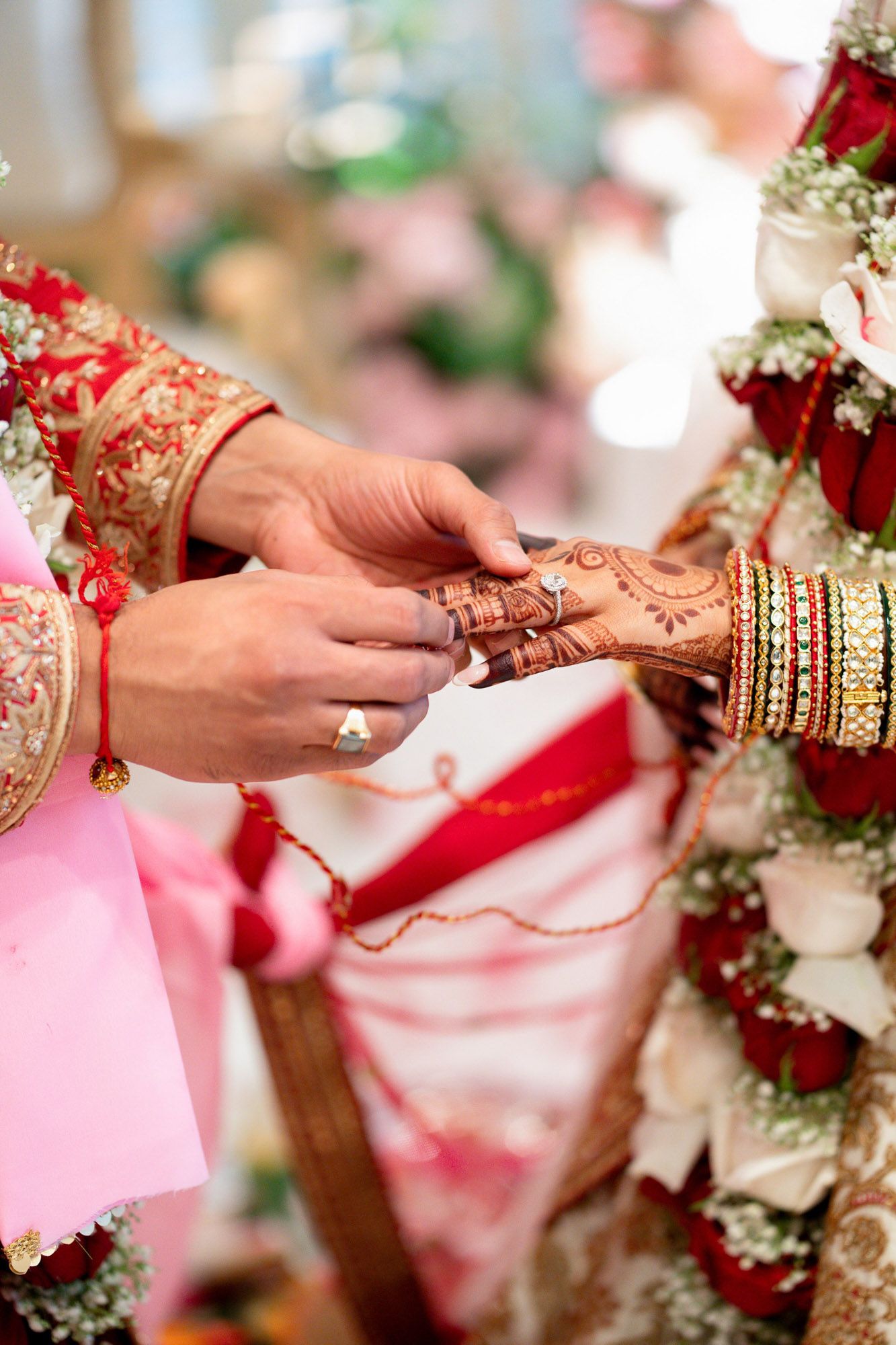 Hands adorned with traditional henna and bangles exchange rings during an Indian wedding ceremony.