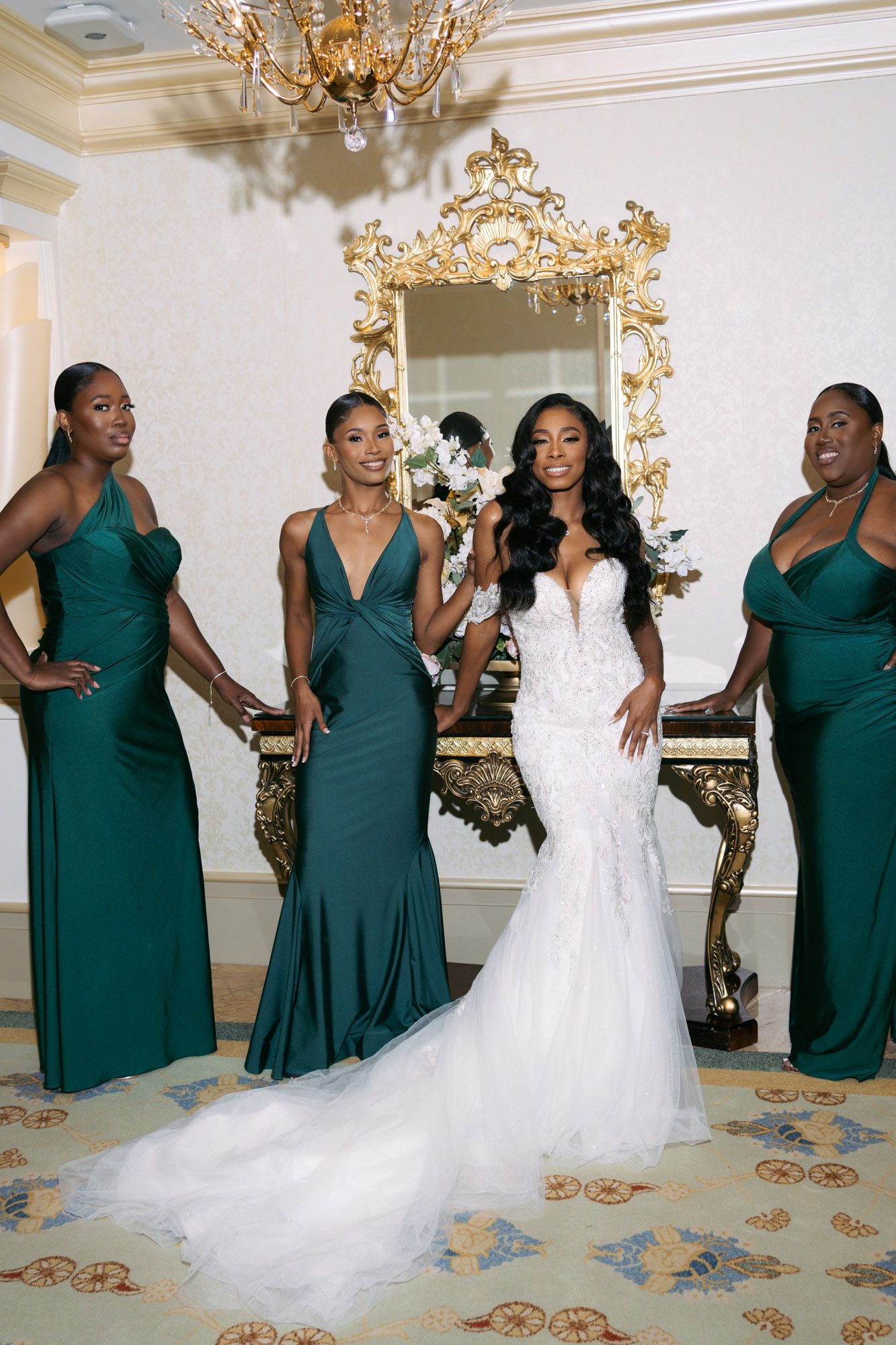 Bridesmaids in emerald green dresses react with joy as they see the bride in her flowing white wedding gown.