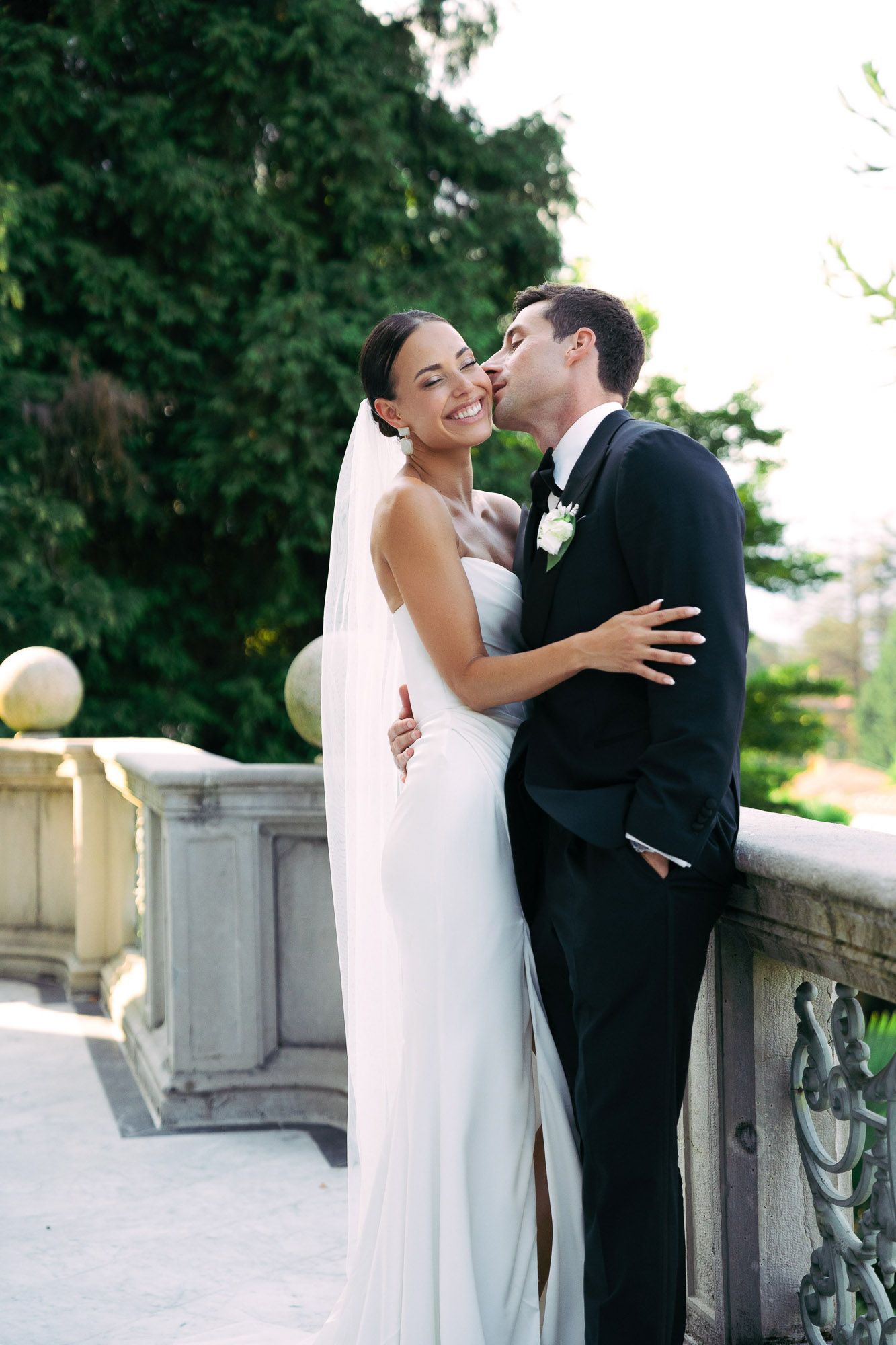A bride and groom share an intimate moment on a stone balcony during their outdoor wedding photoshoot.