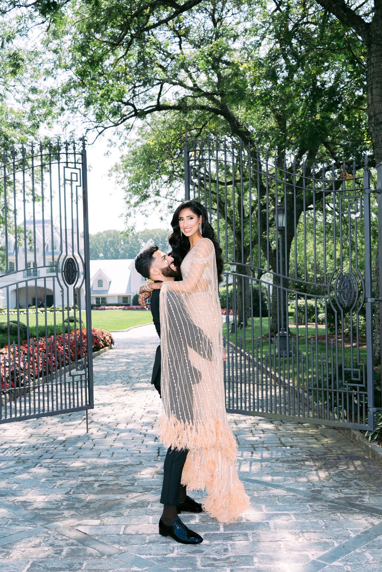 A couple in formal attire dances gracefully in front of an ornate iron gate surrounded by lush greenery.