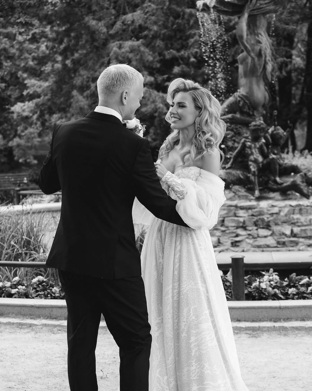 A couple in wedding attire shares a romantic kiss outdoors in black and white photography.