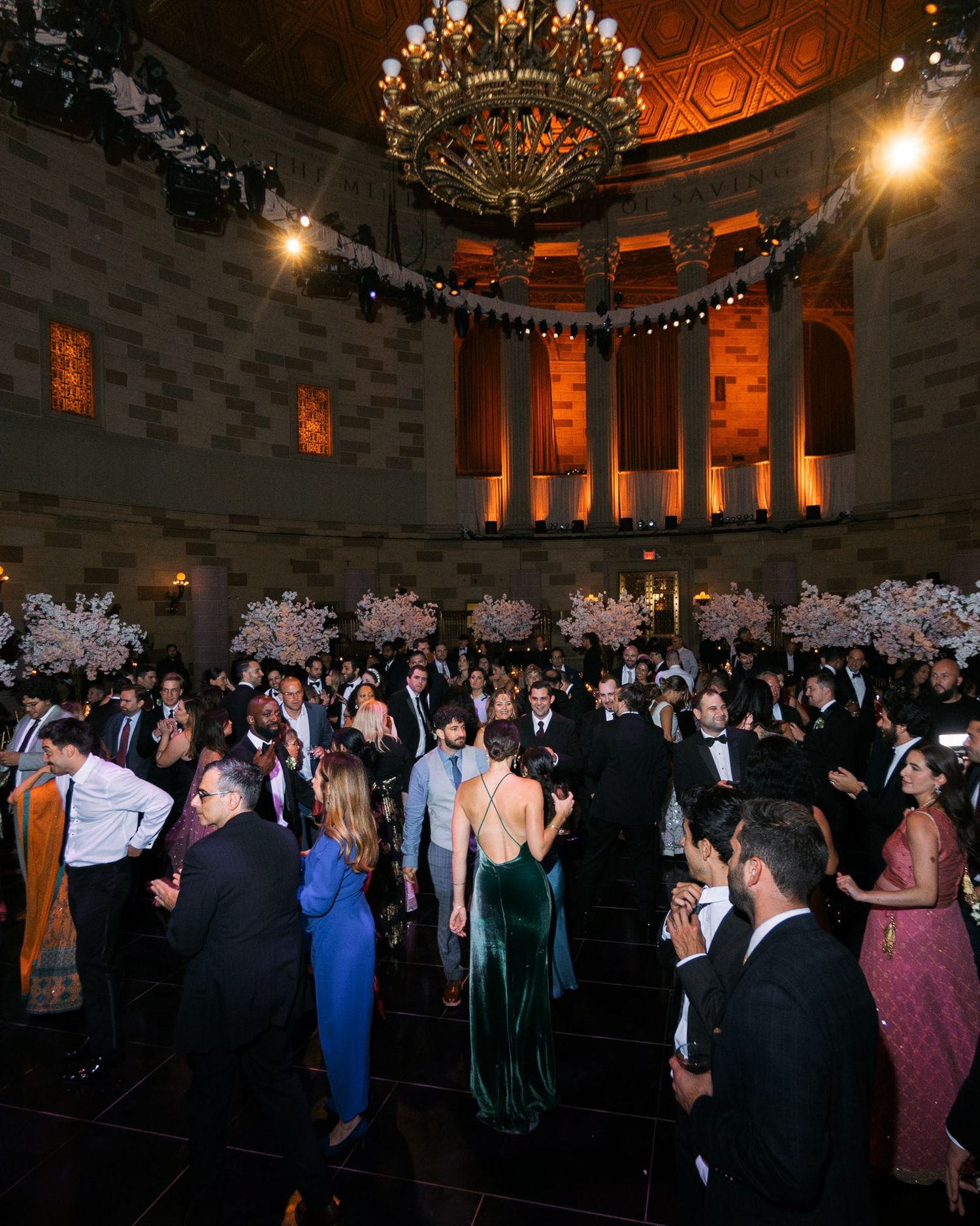 Guests dancing and mingling at an elegant evening reception in a grand ballroom with ornate lighting and architecture.