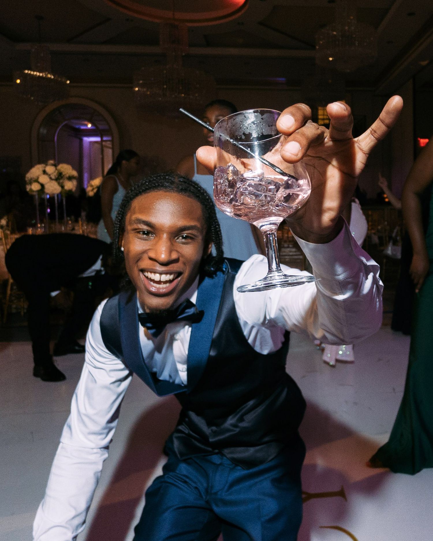 People in formal attire smile and pose while holding cocktail glasses at an evening celebration.