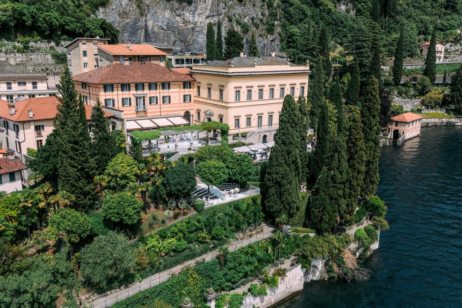 Scenic aerial view of luxury villas and gardens along Lake Como's shoreline in Italy with turquoise blue waters.