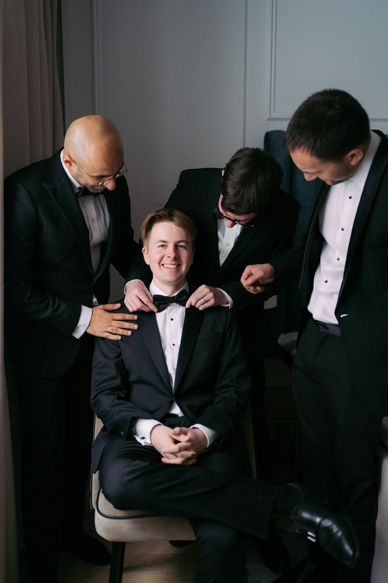 A series of four photos showing groomsmen in black tuxedos and bow ties laughing and sharing a candid moment.