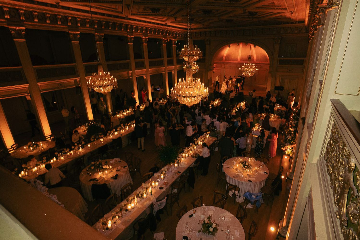 Elegant wedding reception venue with crystal chandeliers and long banquet tables set for dinner in warm lighting.