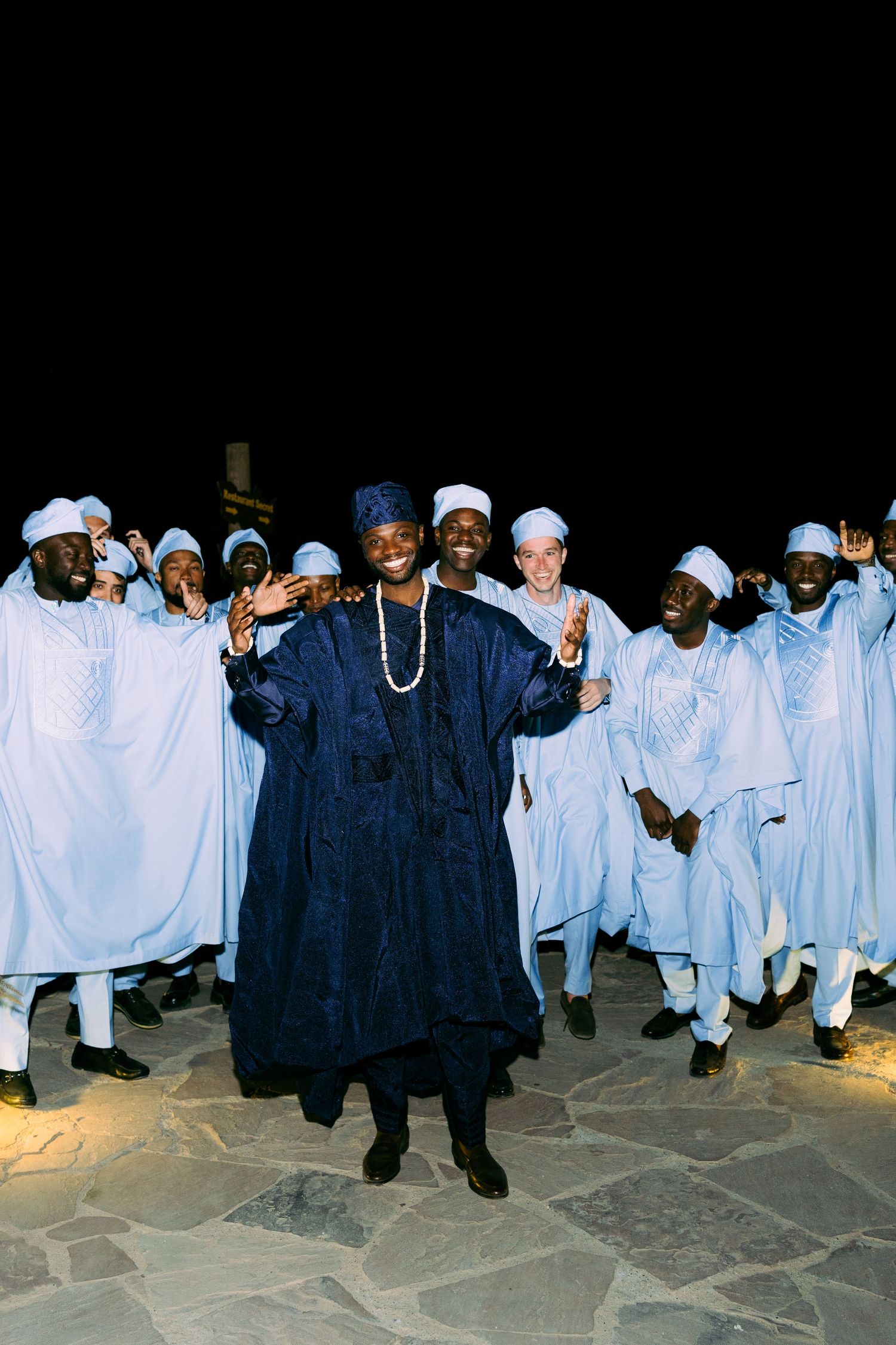 Group of people in traditional blue and white robes gathering for an evening ceremony.