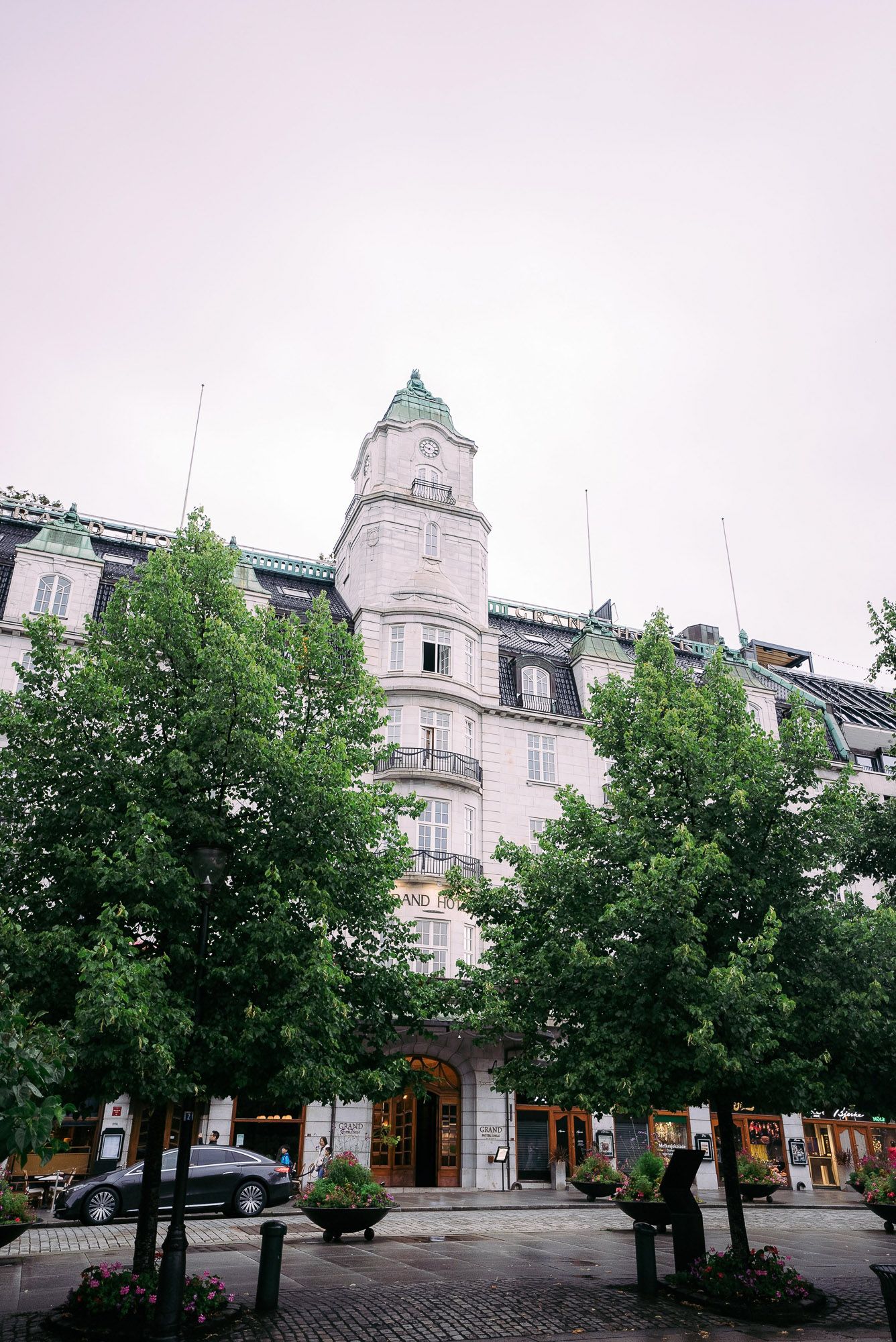Historic white stone building facade with turrets and trees lining a quiet European street.