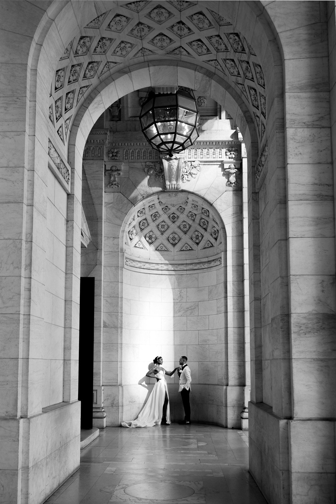Black and white architectural photograph showing ornate arched hallway with decorative ceiling details at New York Public Library.