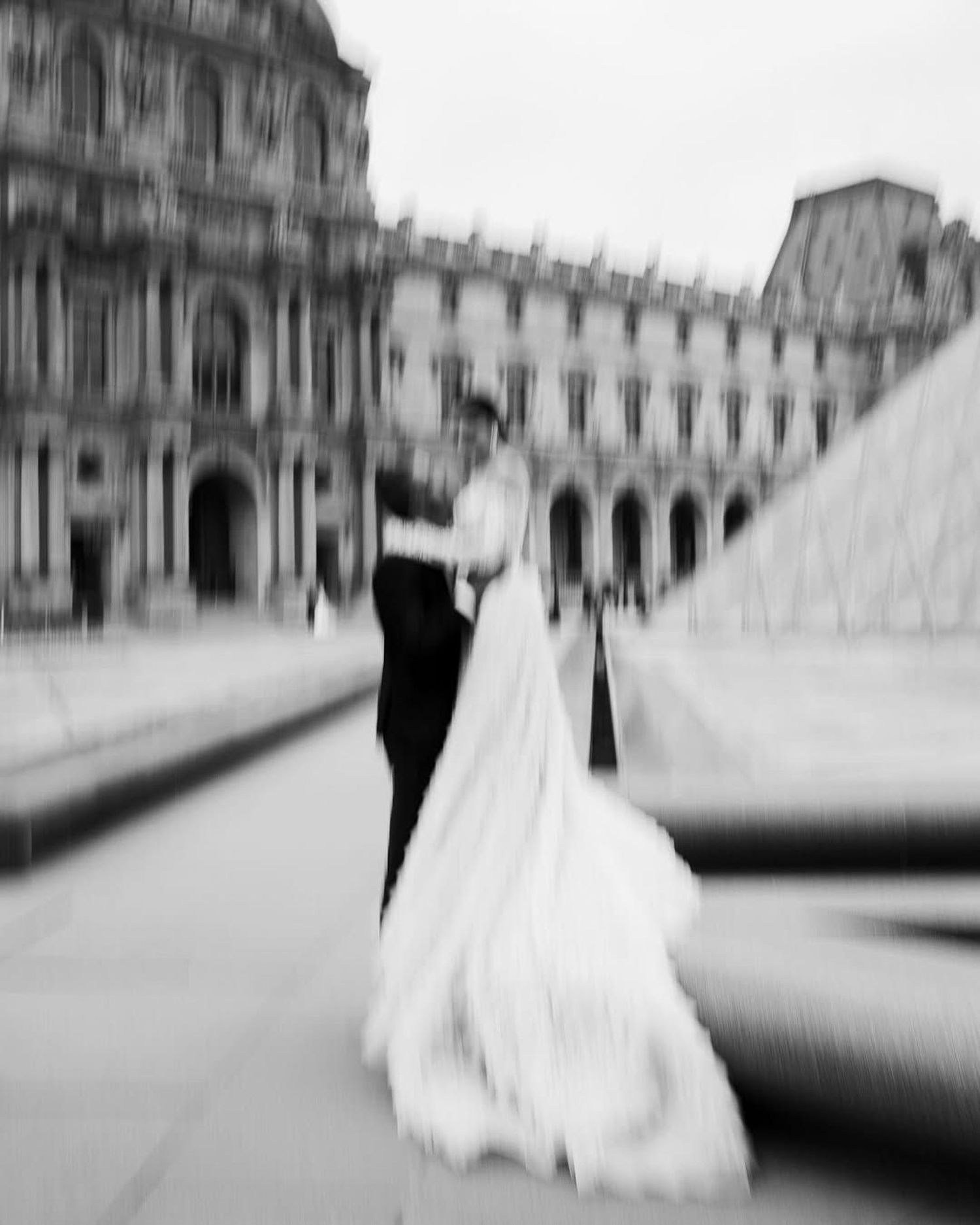 Black and white motion blur sequence of a couple walking across a courtyard in formal wedding attire.