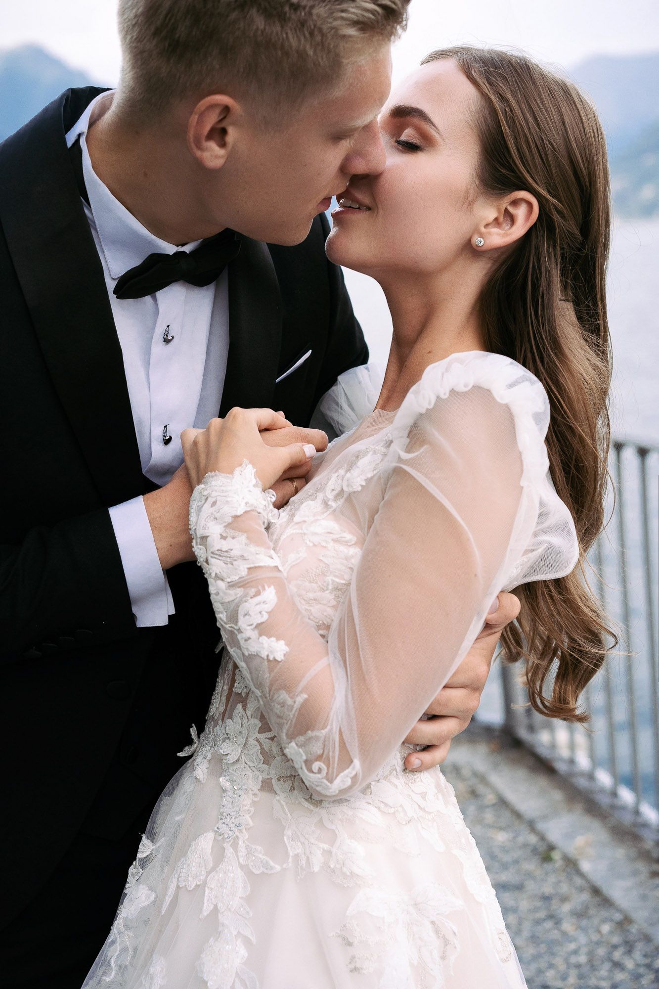 A romantic wedding couple shares an intimate kiss while embracing, with the bride wearing a delicate lace gown.