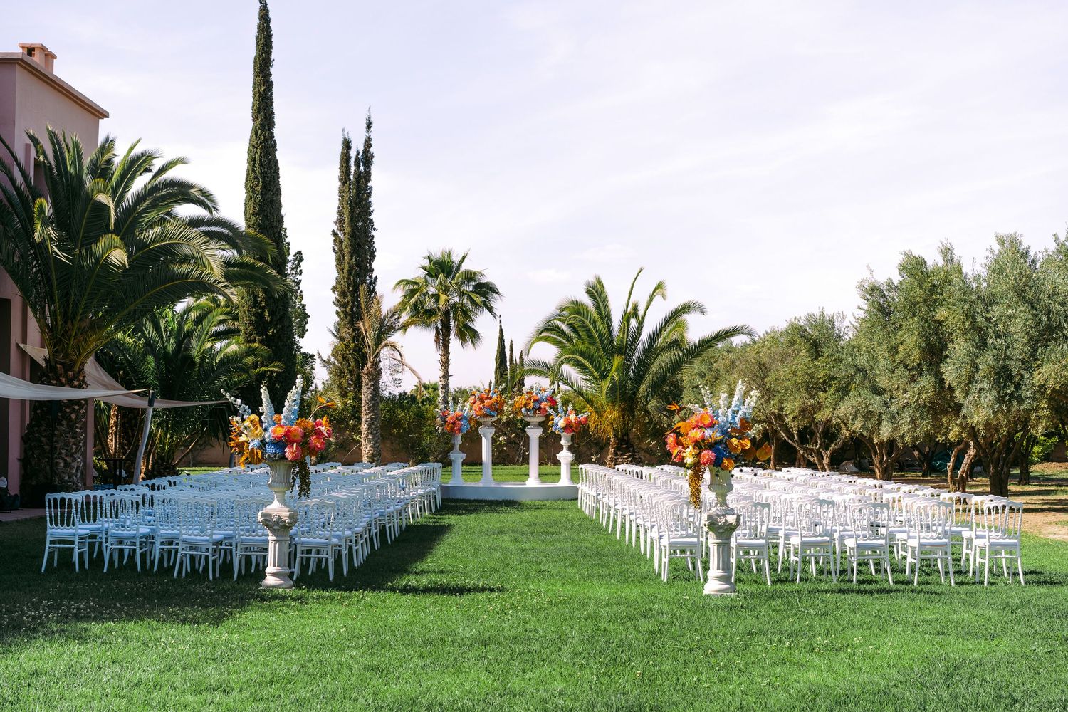 White chairs arranged in rows for an outdoor wedding ceremony surrounded by lush palm trees and cypress landscape.