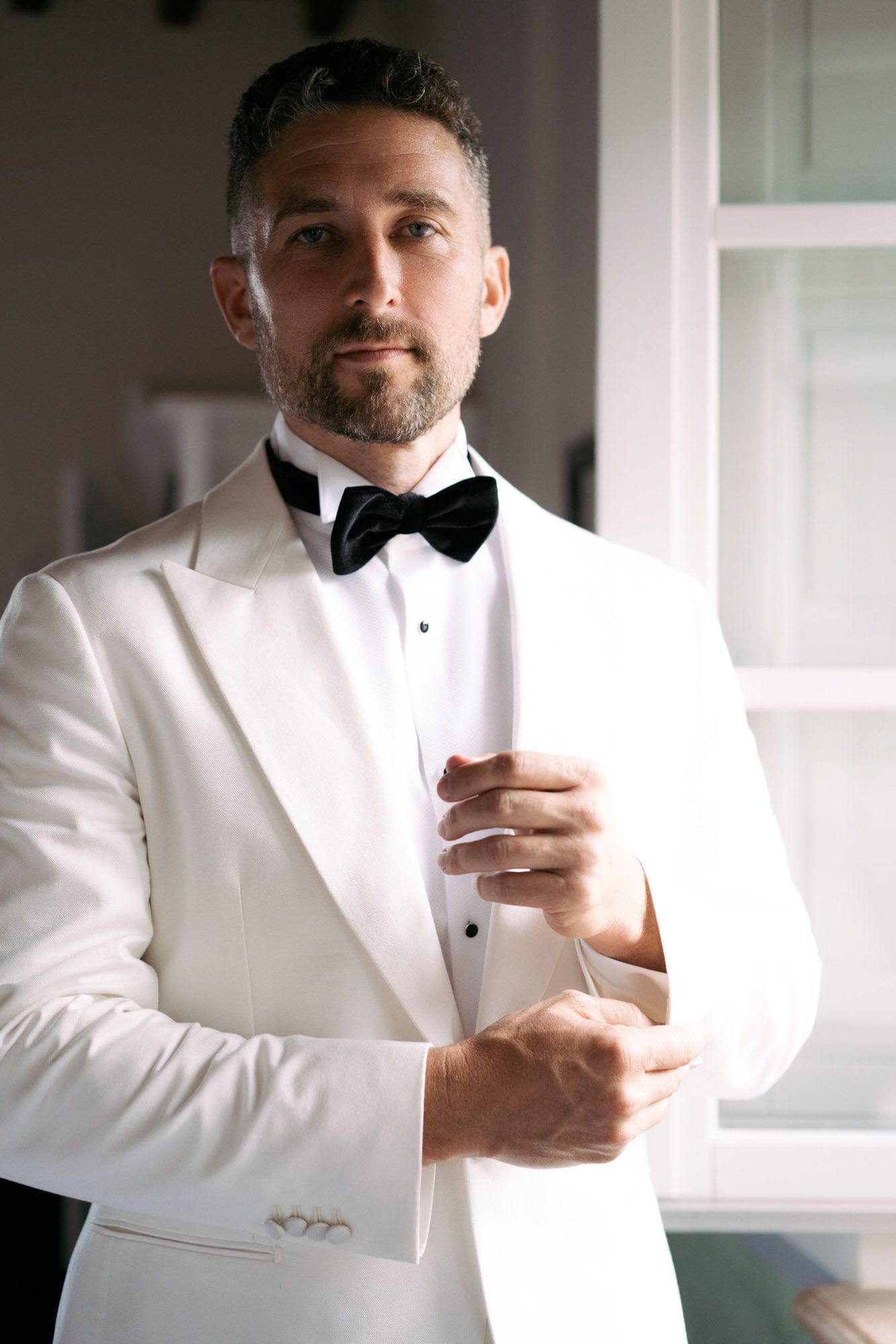 Close-up shots of someone adjusting their formal white tuxedo jacket and bow tie while getting dressed.