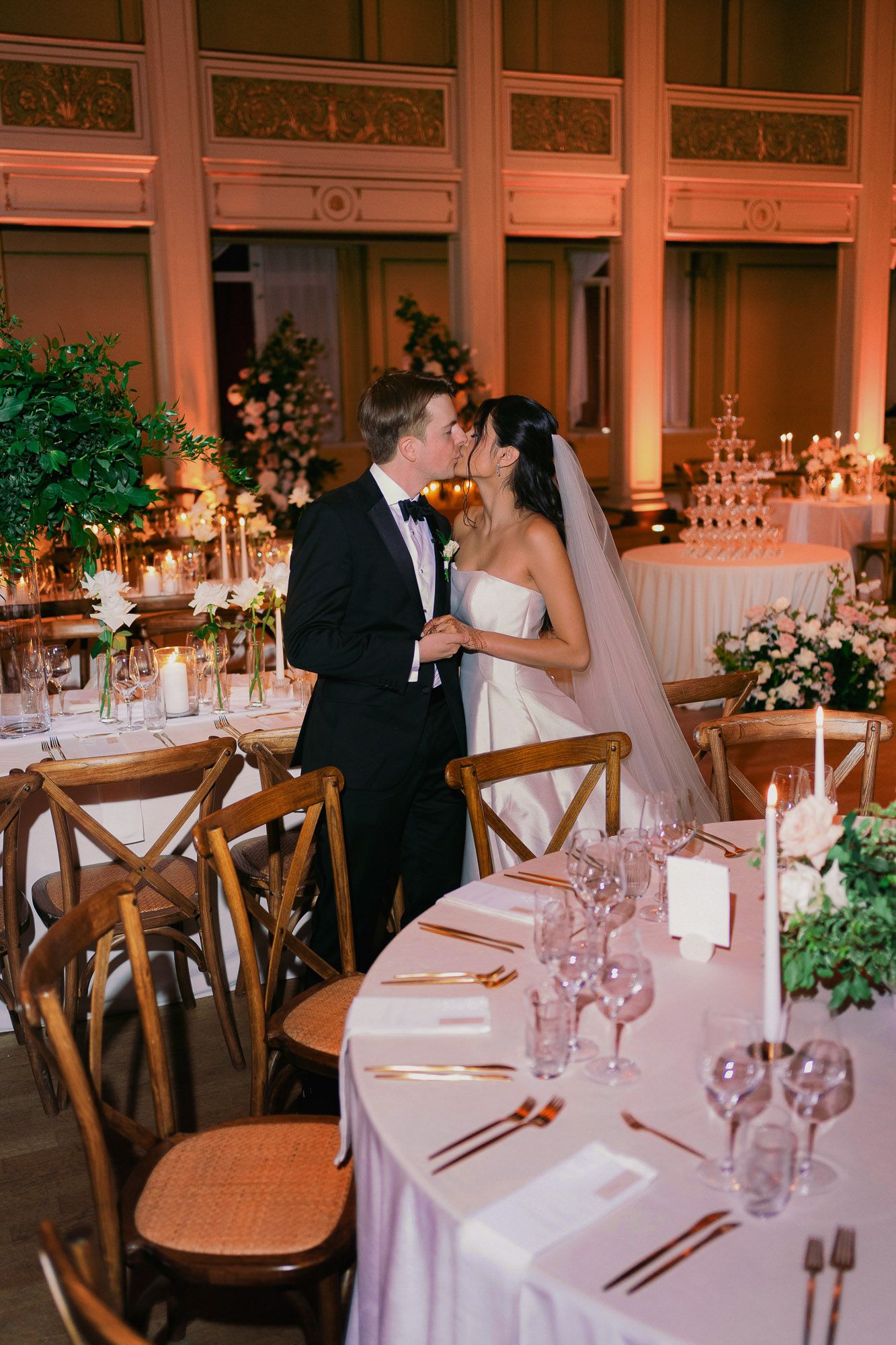 Elegant wedding reception tables decorated with candlelight, floral arrangements and wooden chairs in a romantic venue.