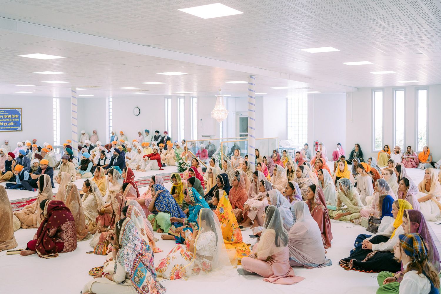 People in traditional attire gather in a bright indoor space for a cultural or religious ceremony.