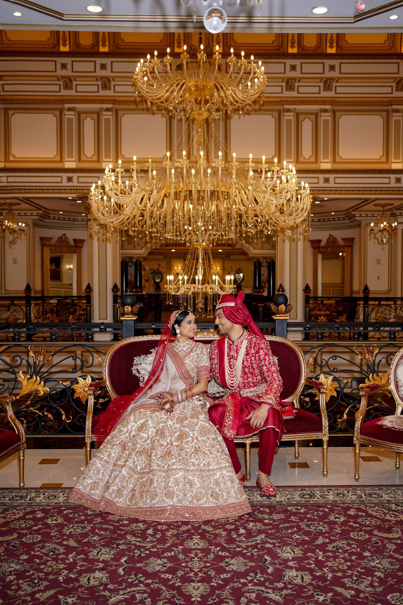Luxurious ballroom with crystal chandeliers and ornate decor featuring traditional Indian wedding attire on display.