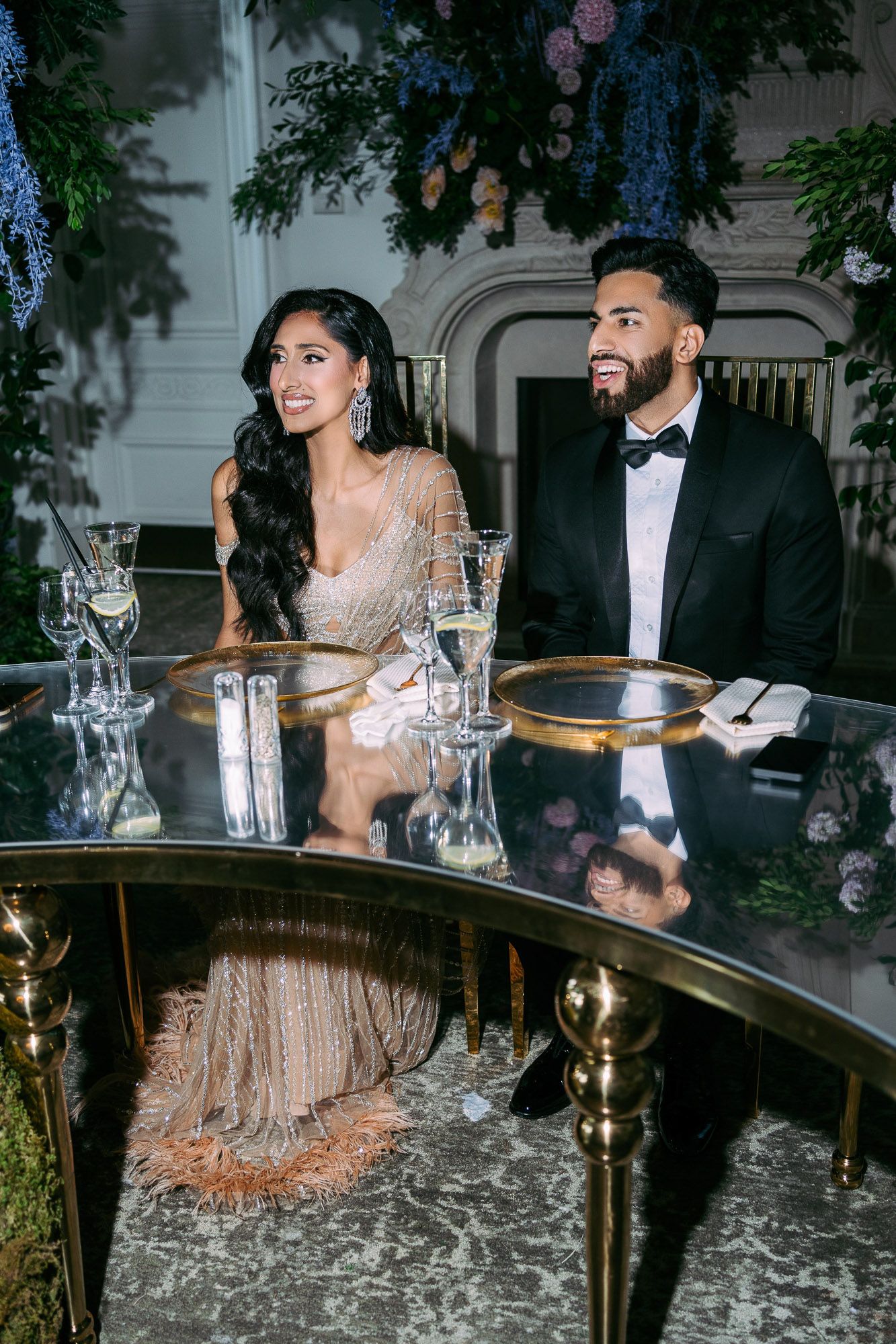 Elegant couple in formal attire enjoying dinner at a luxurious outdoor reception with romantic lighting and table settings.