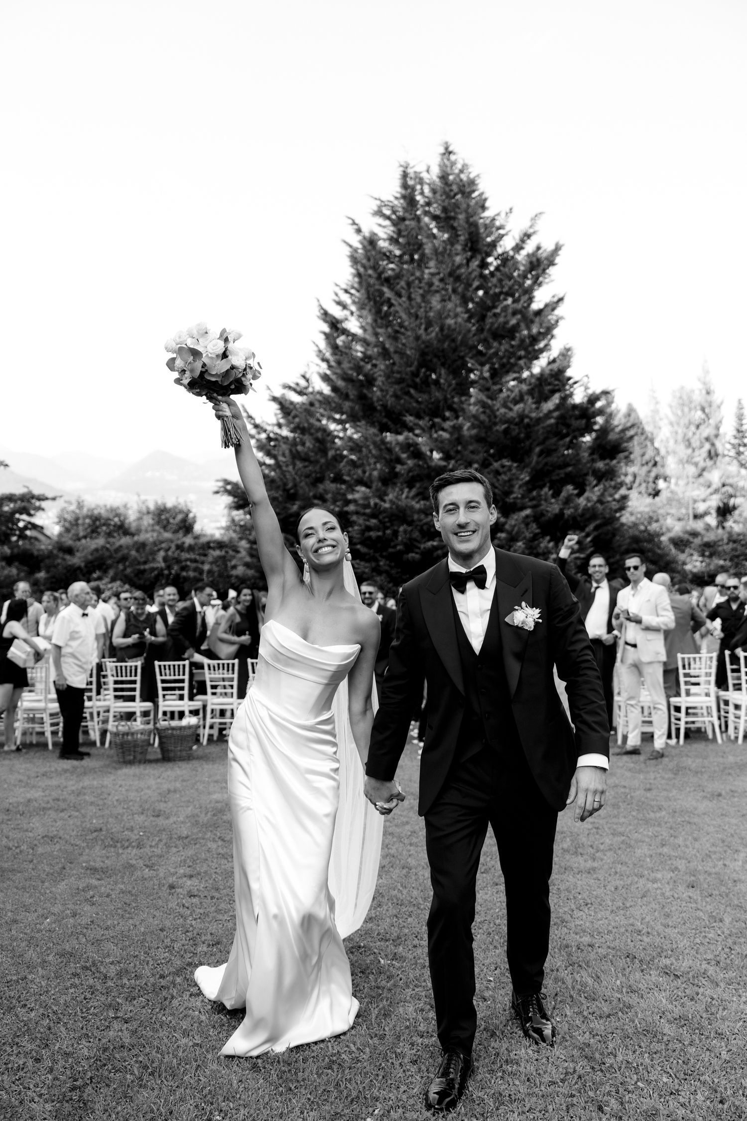 A joyful couple walks across a grassy lawn during their outdoor wedding celebration.