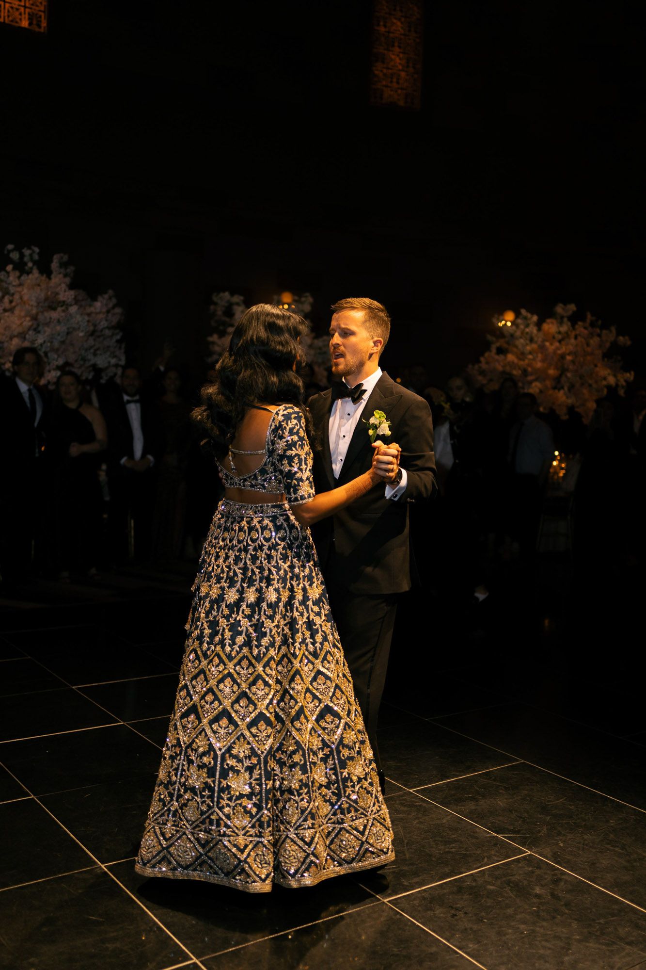 A couple dances on a dark floor, with the woman wearing an ornate black and white patterned ballgown.