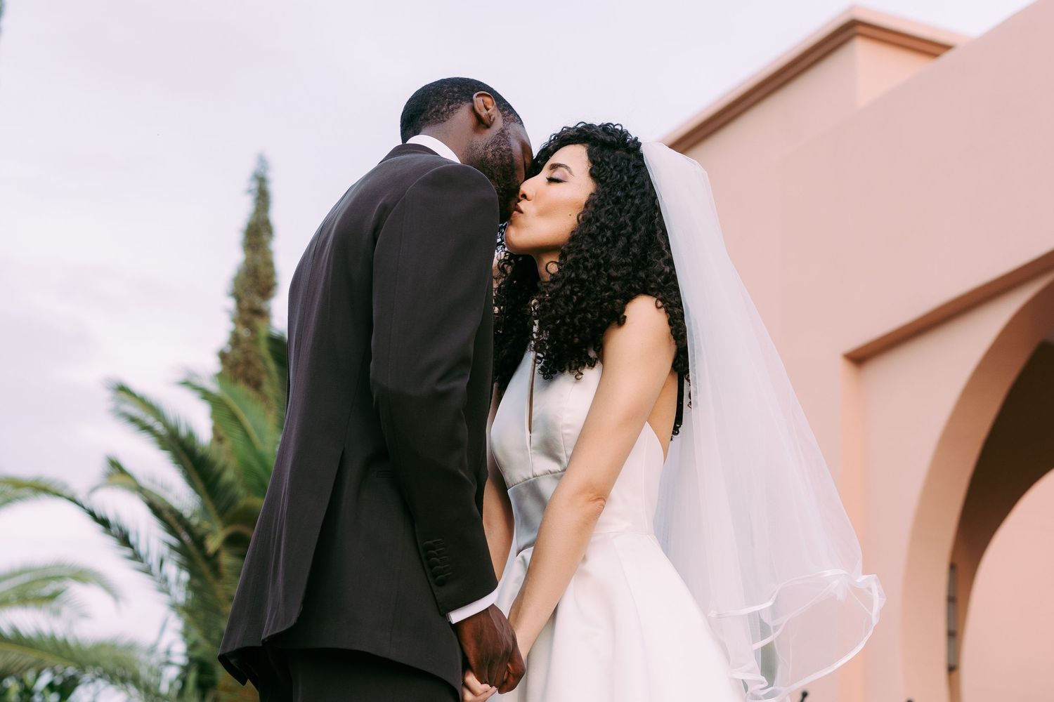A romantic wedding moment captured against a terracotta wall with palm trees in the background.