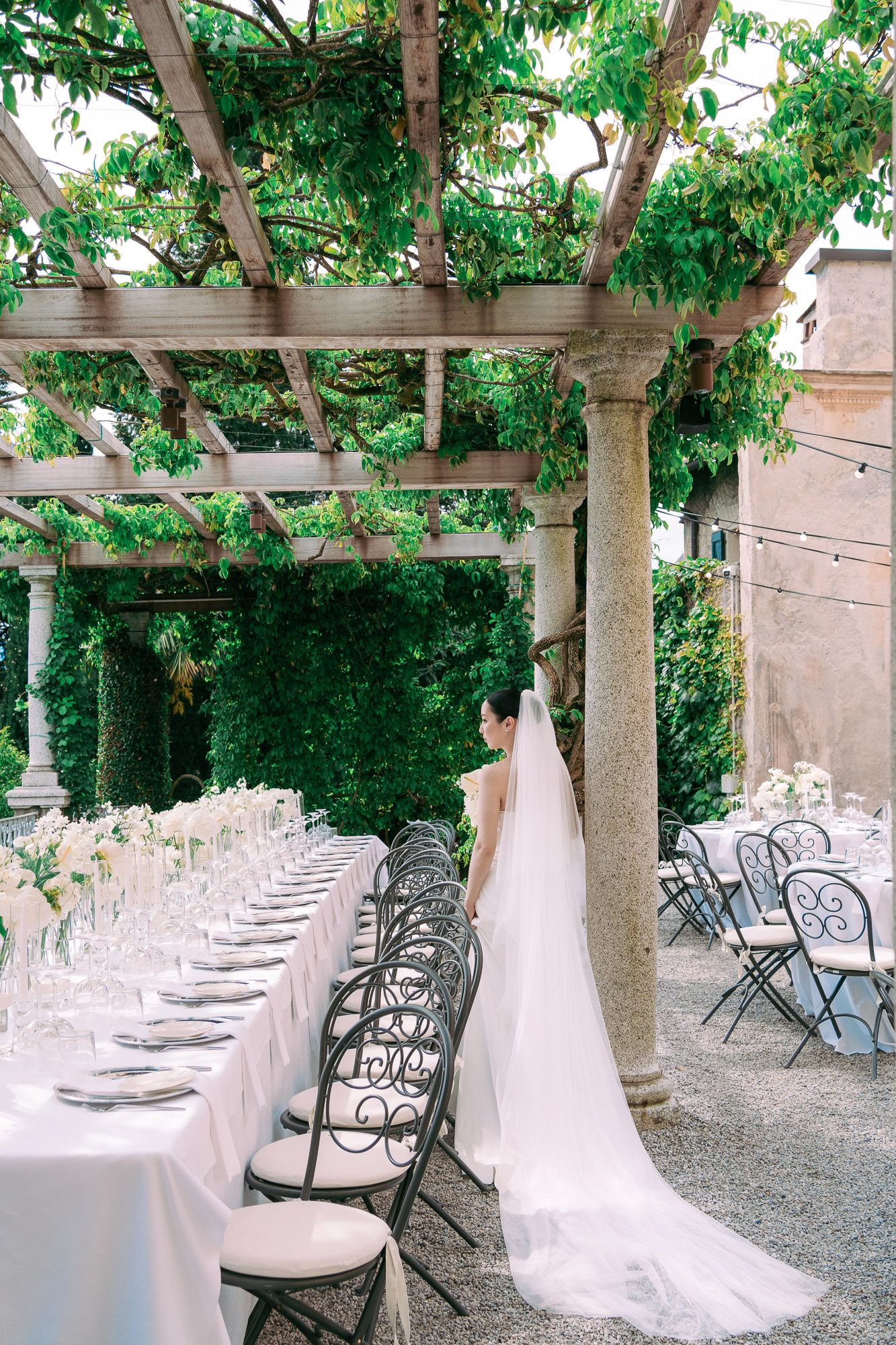 Elegant outdoor wedding reception setup with white tablecloths and chairs under trees creating a romantic garden atmosphere.