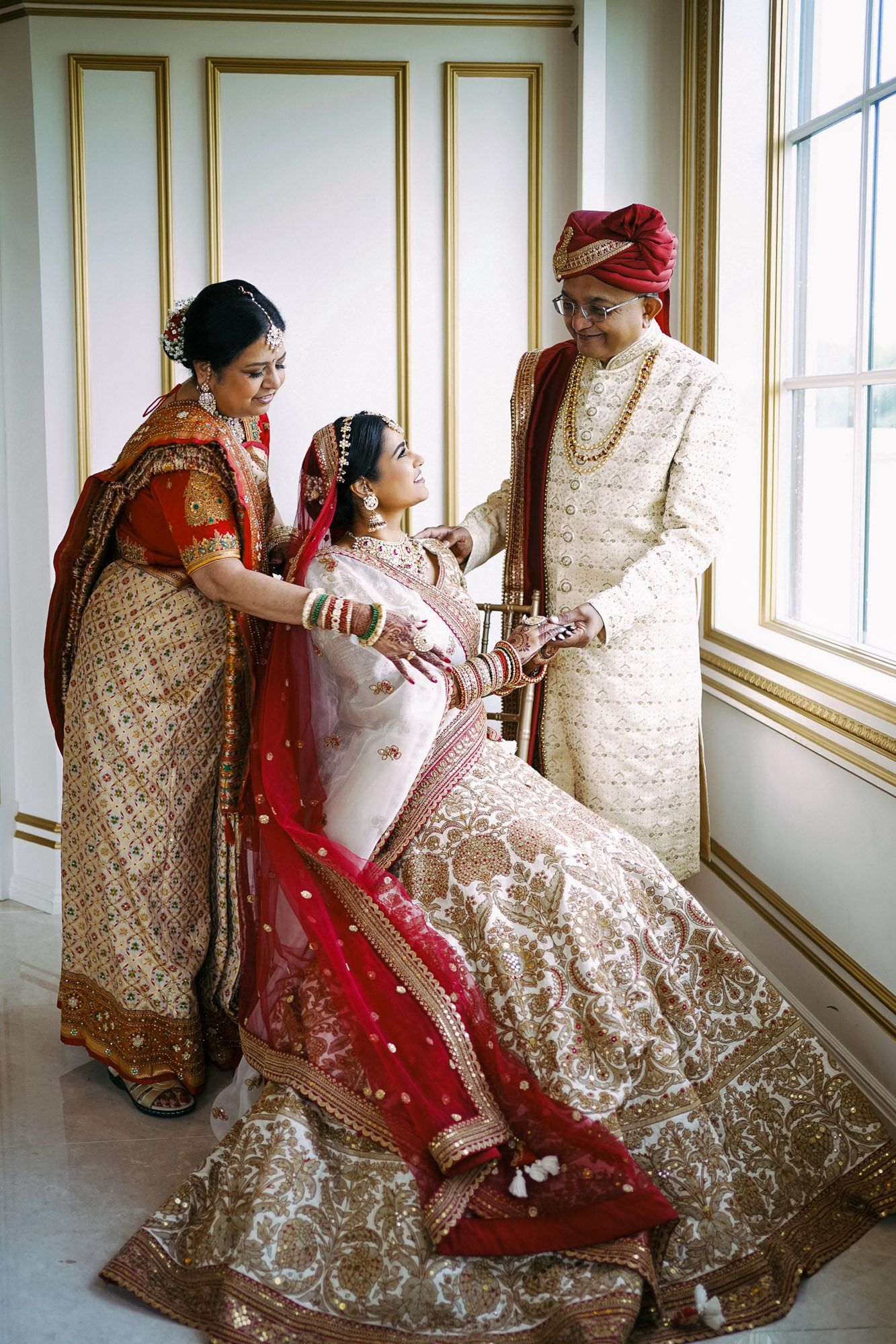 Traditional Indian wedding attire featuring ornate lehengas in red and gold with intricate embroidery details near bright windows.