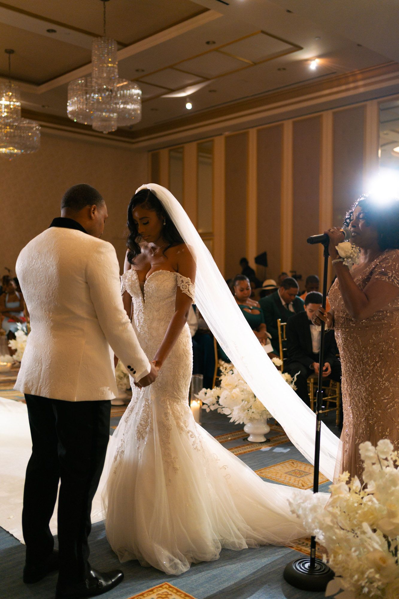 Wedding dress display at a bridal show featuring multiple white gowns with elegant details and crystal chandeliers overhead.