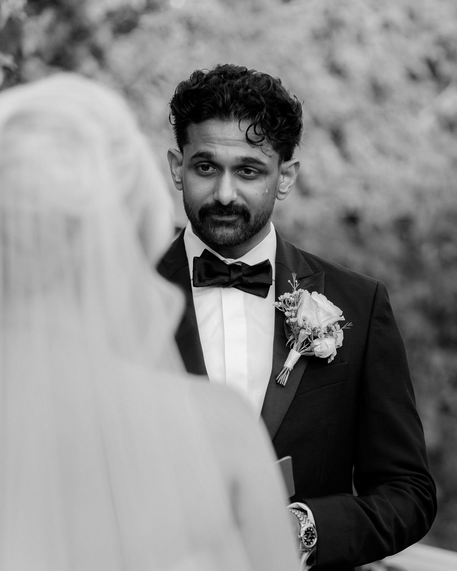 A black and white wedding photo capturing an emotional moment between two people in formal attire.