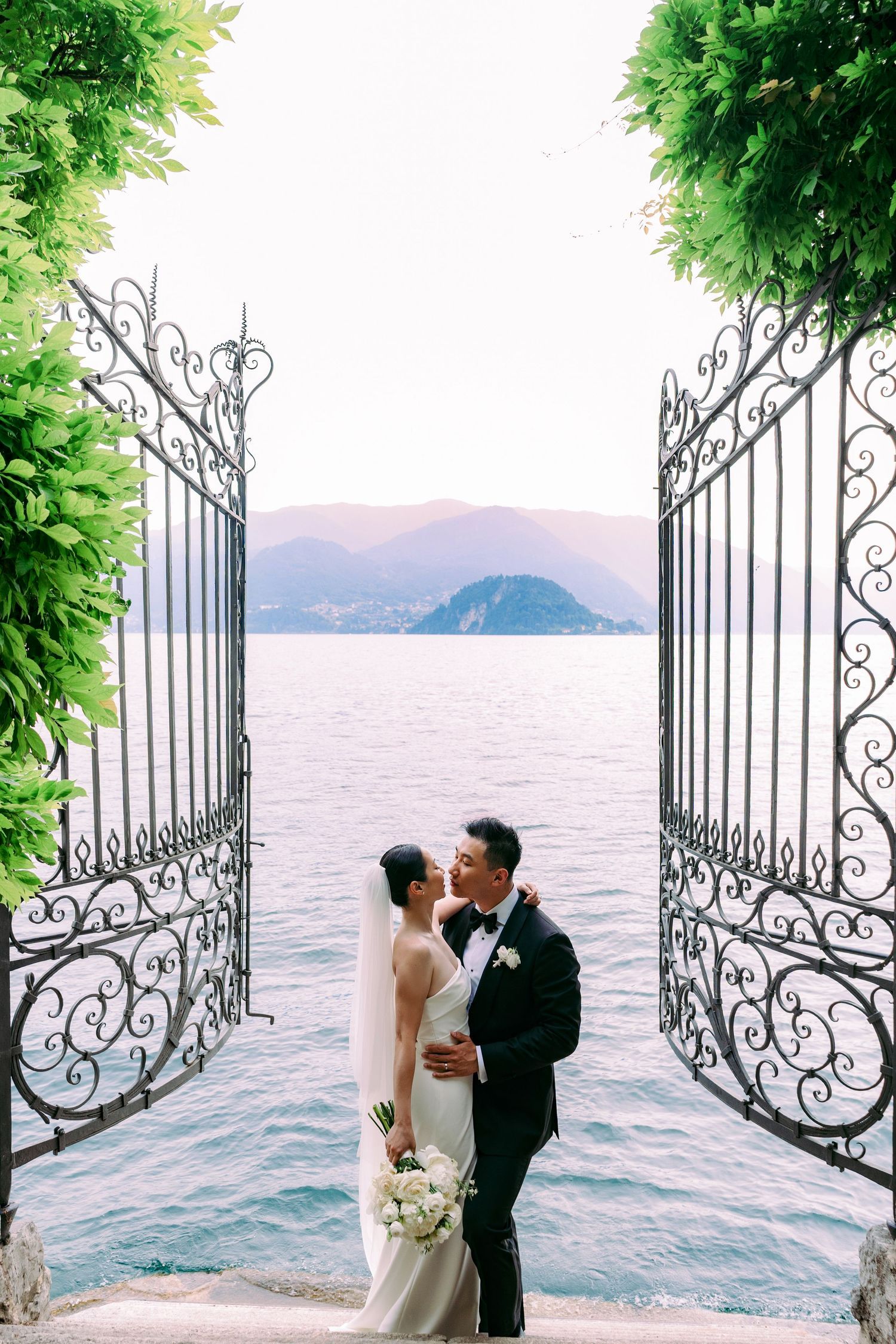 Ornate iron gates frame a romantic lakeside scene with mountains and water at Lake Como, Italy.