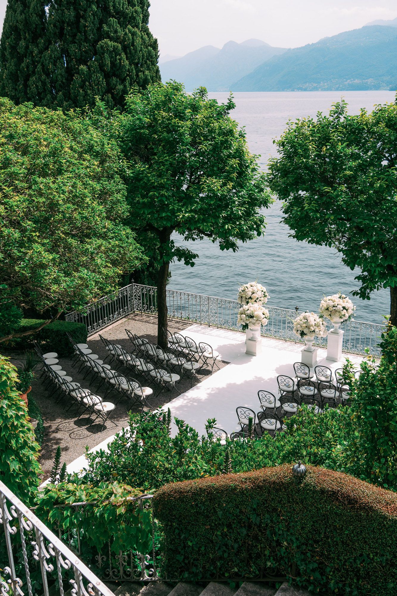 Elegant lakeside wedding ceremony setup with white chairs and floral arrangements overlooking mountains and water.