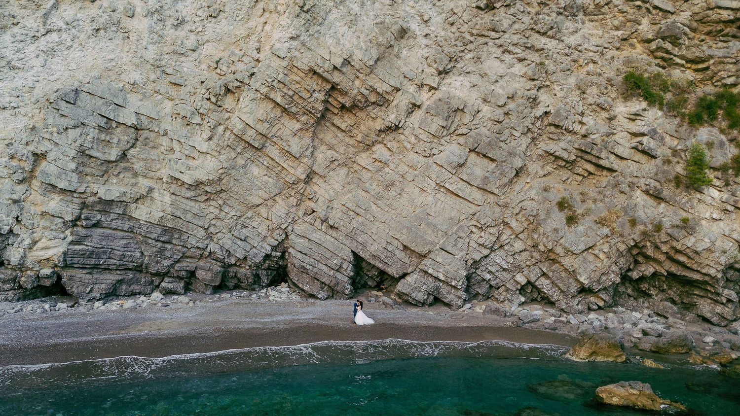 Panoramic view of rugged coastal cliffs with turquoise waters and rocky beach formations along a Mediterranean shoreline.