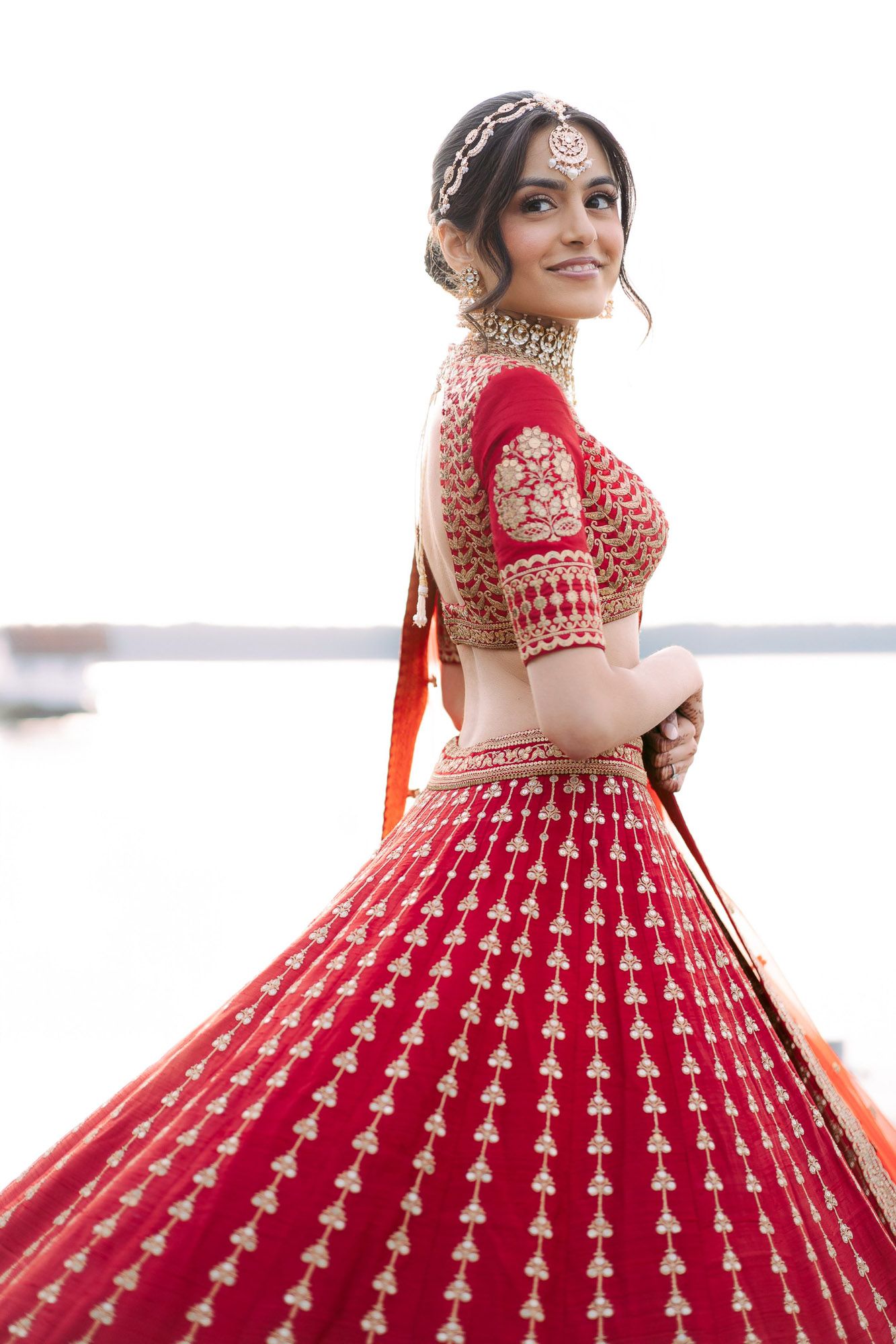 A bride in a stunning red and gold lehenga twirls to show off the intricate details of her dress.
