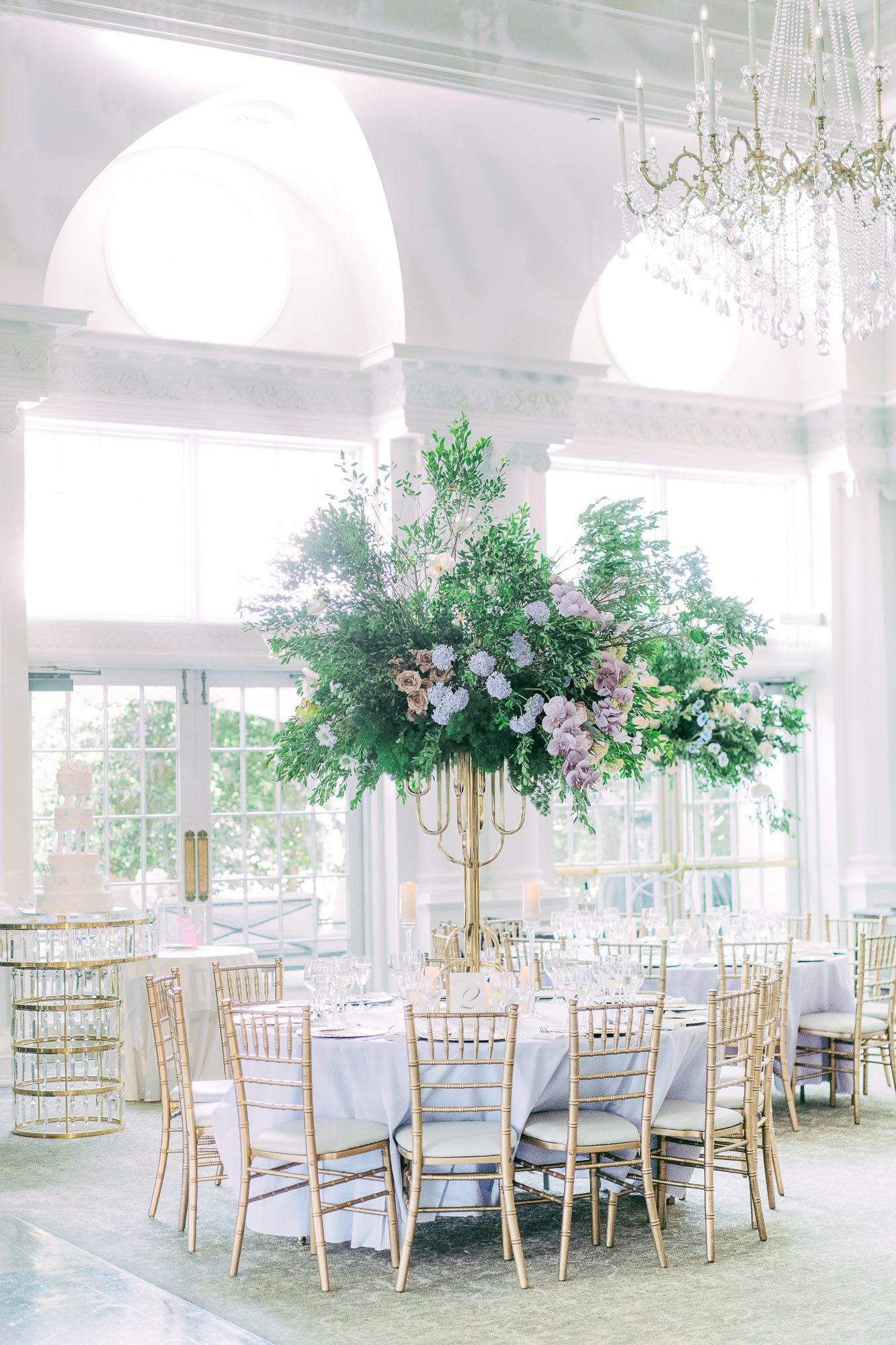 Elegant wedding reception venue with white columns, gold chiavari chairs and lush floral centerpieces in an airy space.