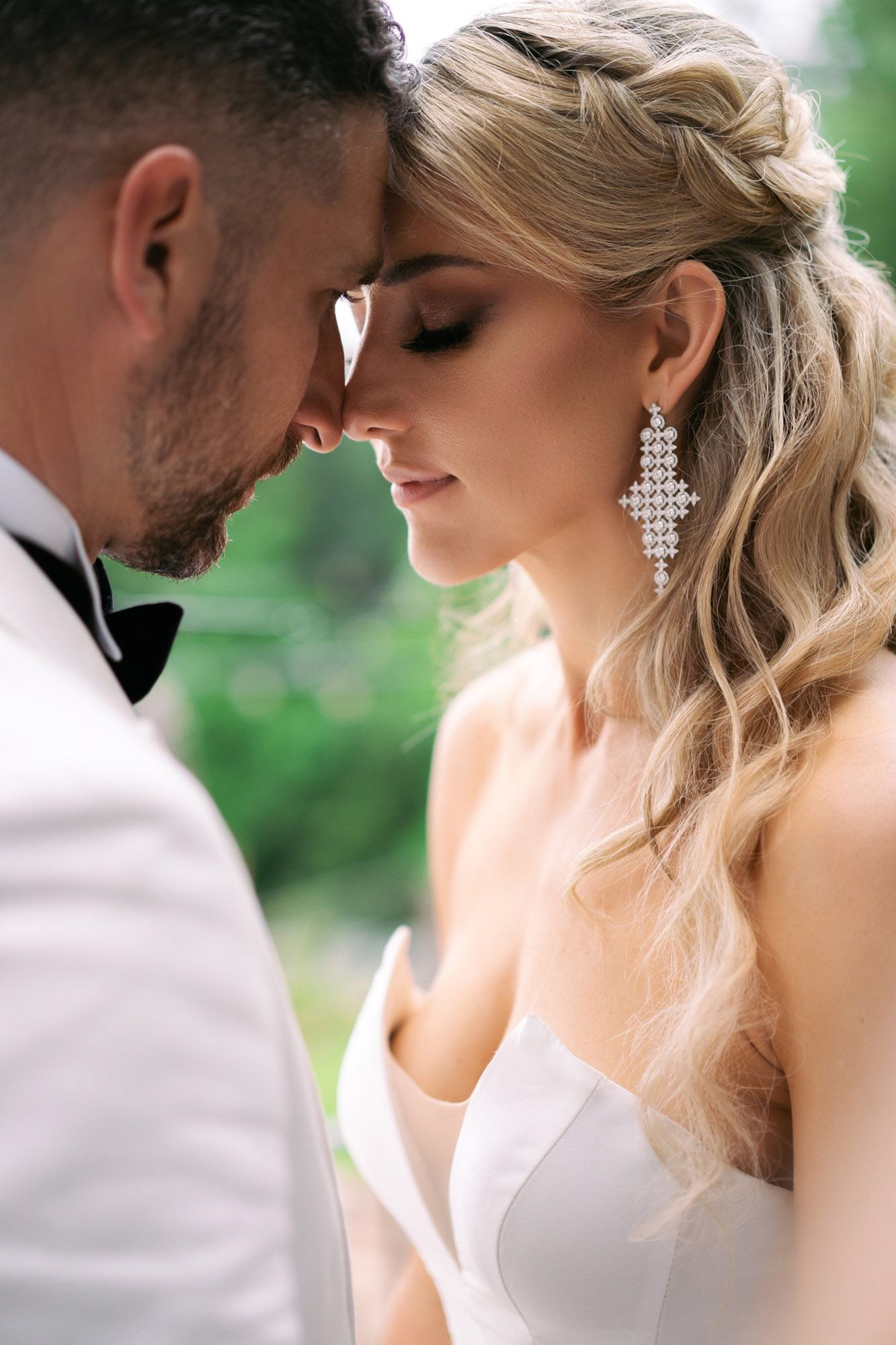 A romantic couple in wedding attire share an intimate moment against a soft green outdoor background.