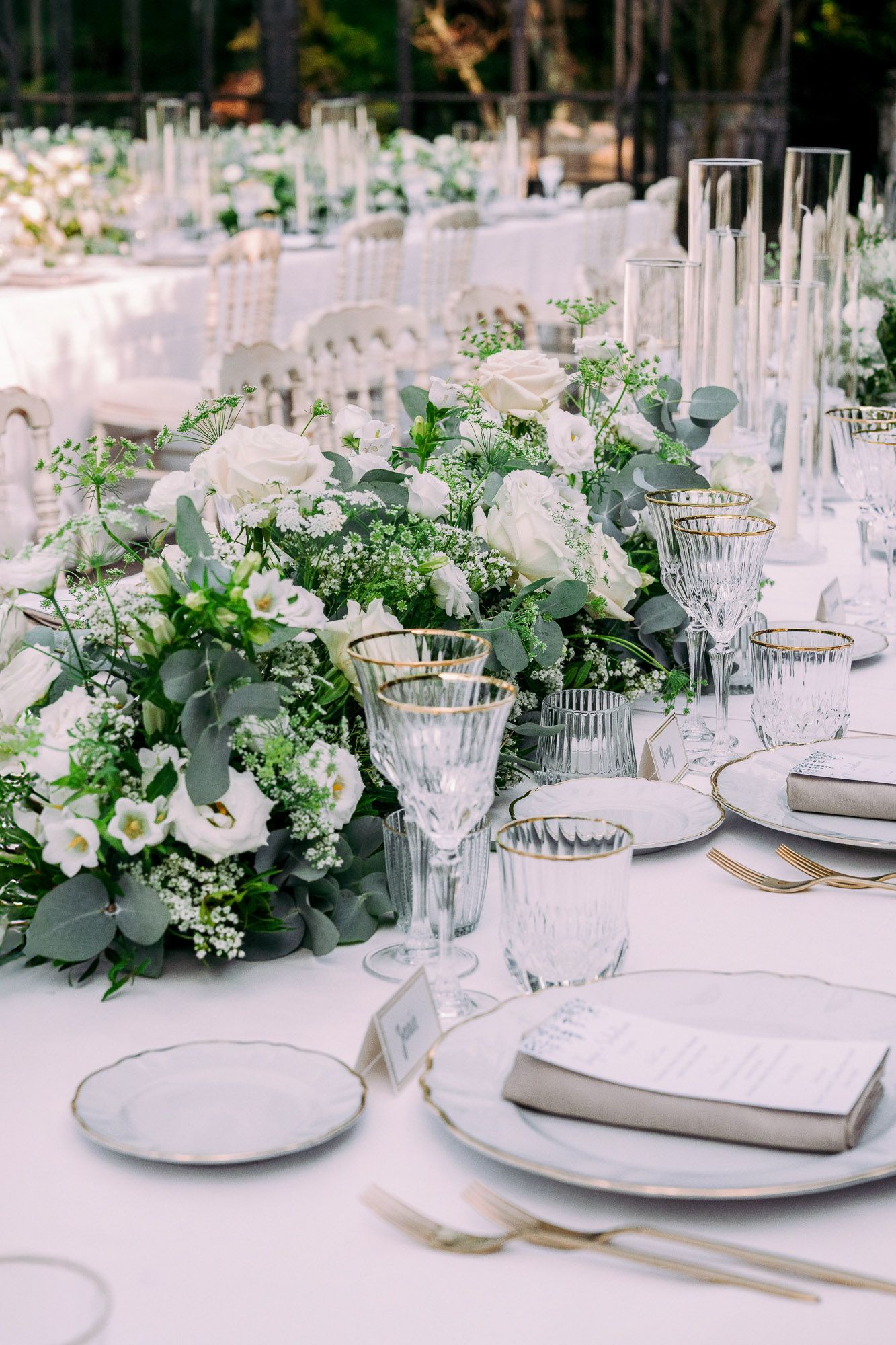 Elegant wedding table settings with white floral centerpieces, crystal glassware, and eucalyptus greenery create a romantic atmosphere.