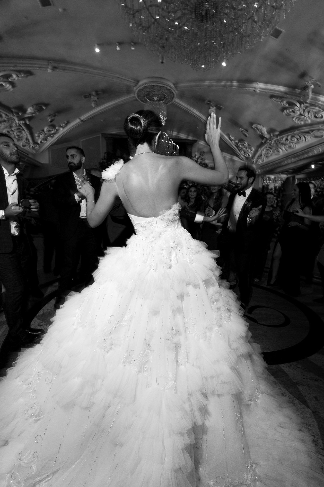 A bride in a dramatic ruffled ballgown twirls on the dance floor during a wedding reception celebration.
