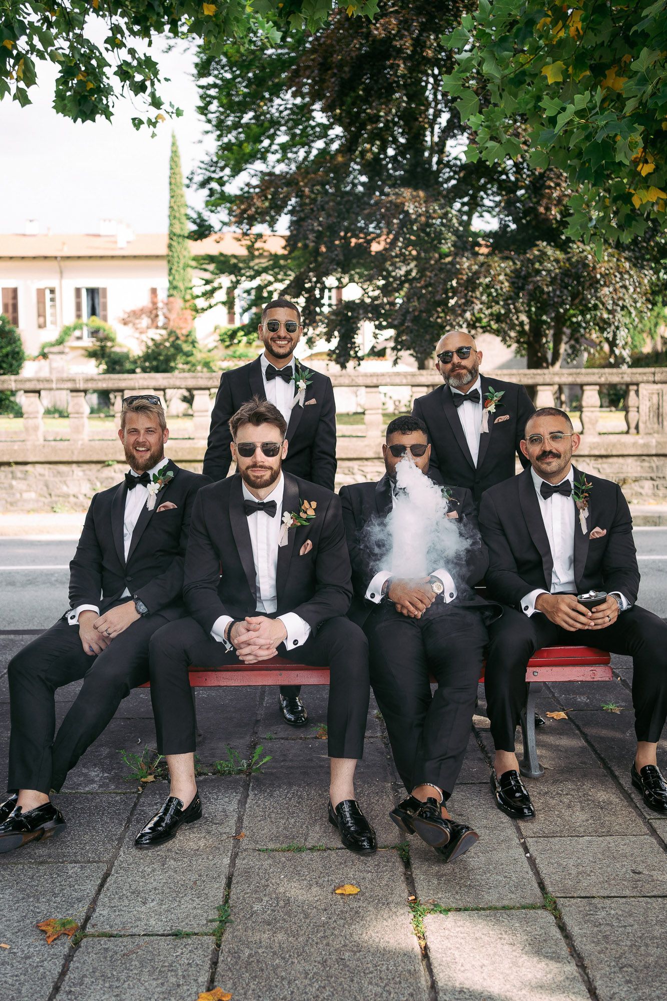 A group wearing black suits and sunglasses sit casually on concrete steps in a progressive sequence of photos.