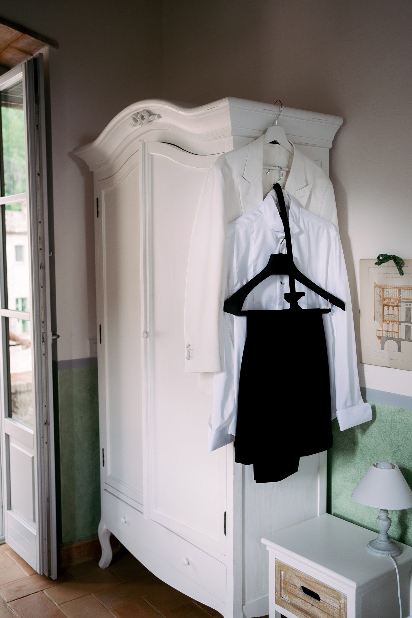 White wardrobe cabinet with hanging clothes and black garments displayed in a room with mint green walls.