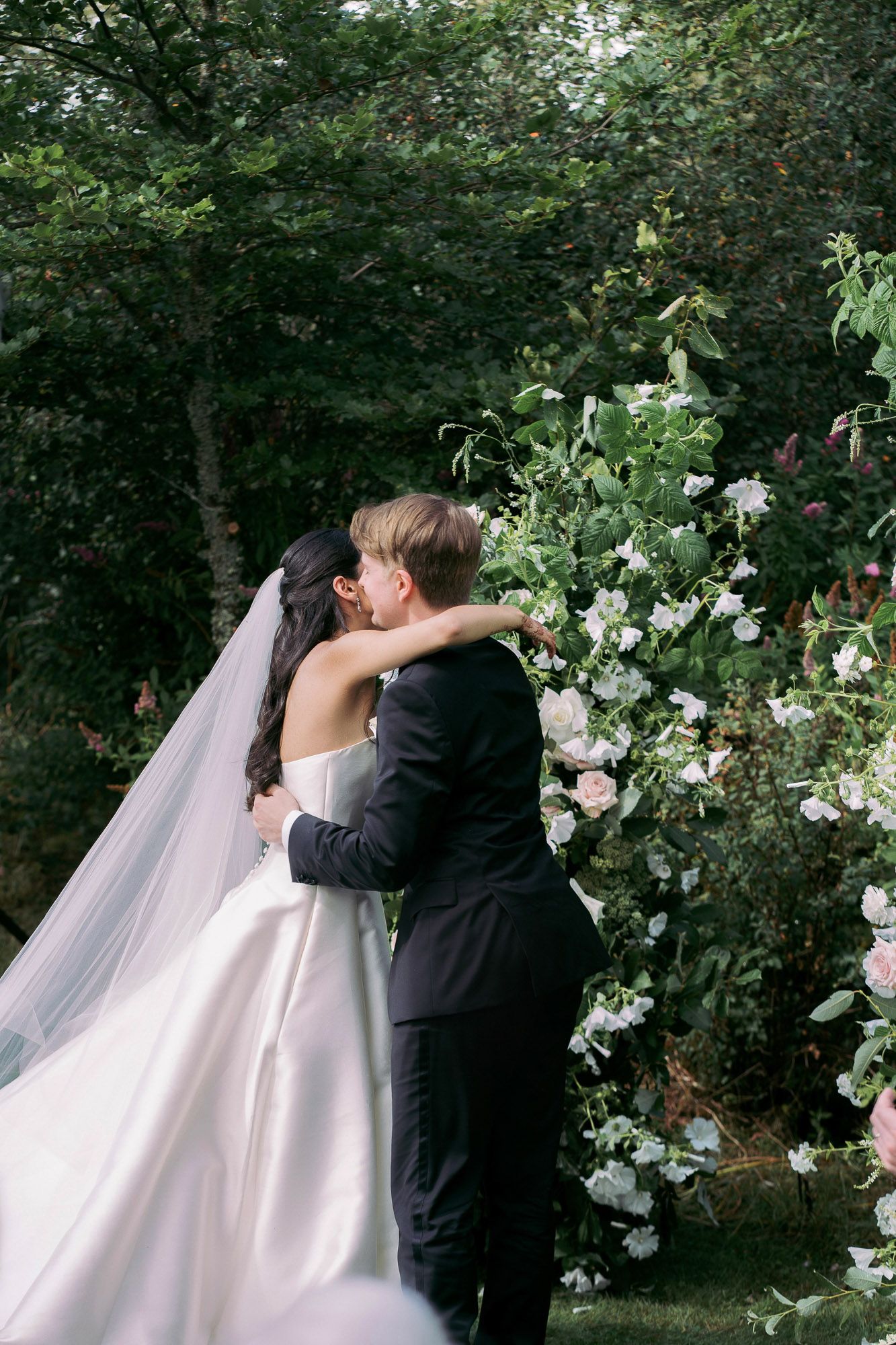 A romantic wedding kiss sequence in a lush garden setting with white flowers and greenery.