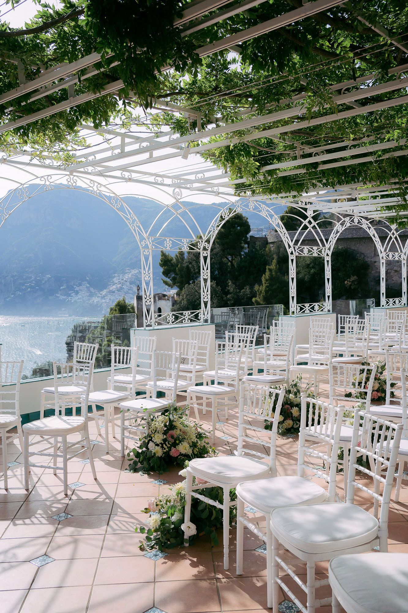 White chairs arranged for an outdoor wedding ceremony under a pergola overlooking a scenic mountain lake view.