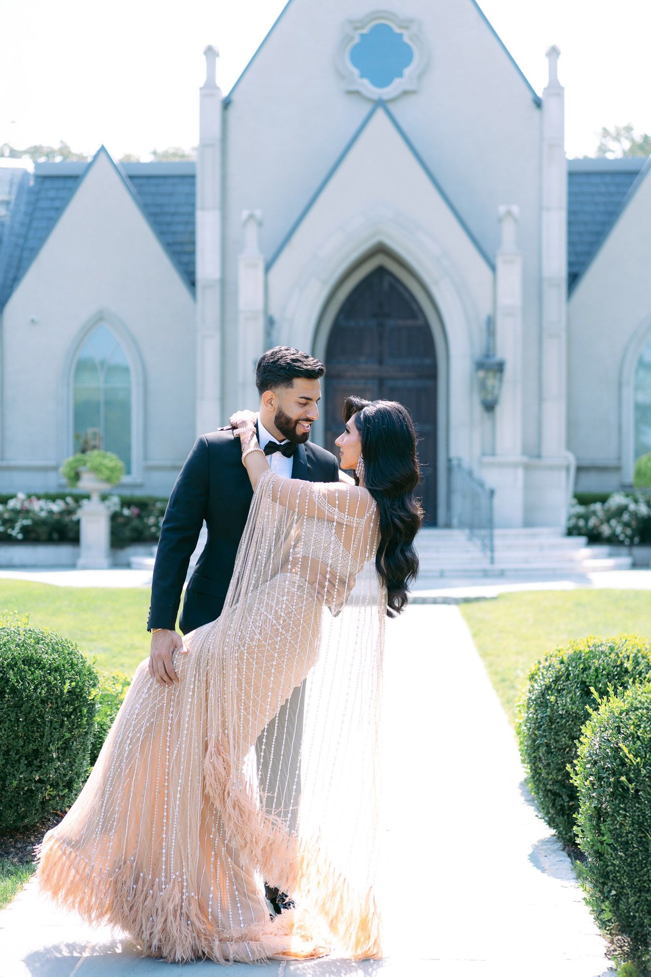 A romantic couple poses for wedding photos in front of a white Gothic-style church with elegant architecture.