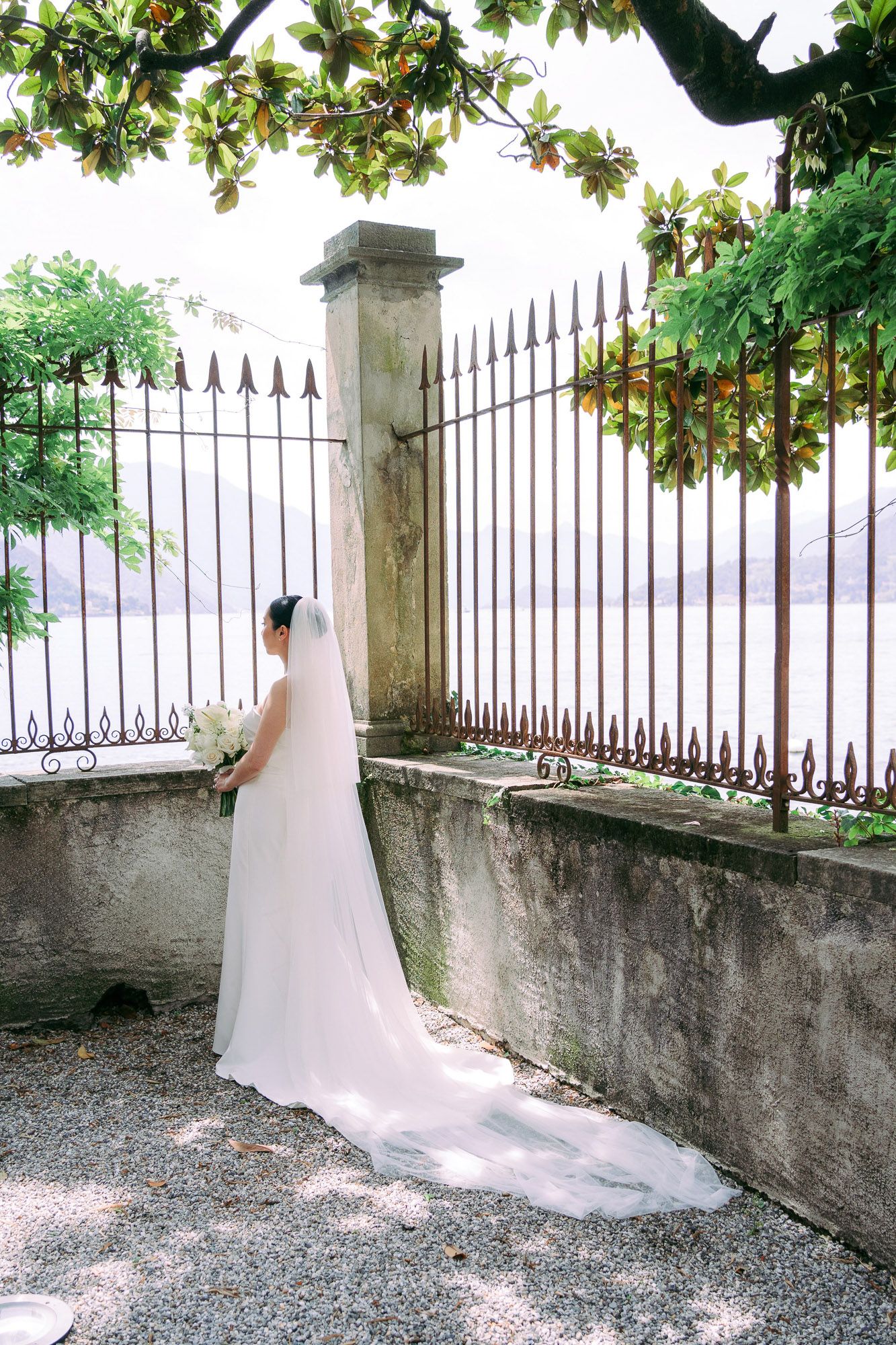 Wedding photos captured along an ornate iron fence with trailing bridal gown and veil against stone wall.