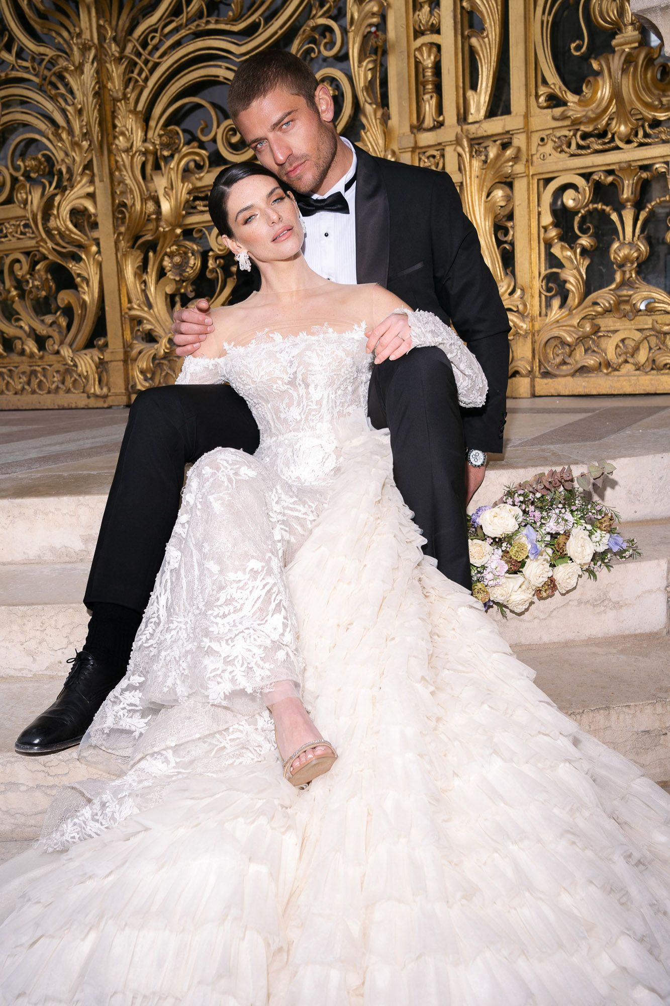 Romantic wedding couple in formal attire dancing gracefully against an ornate gold backdrop.